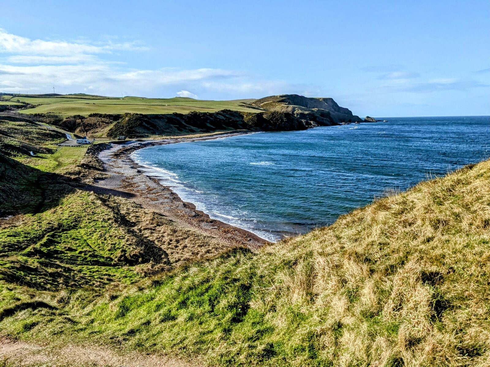 The pebble beach at Aberdour Bay backed by red sandstone cliffs and sea caves, Aberdeenshire.