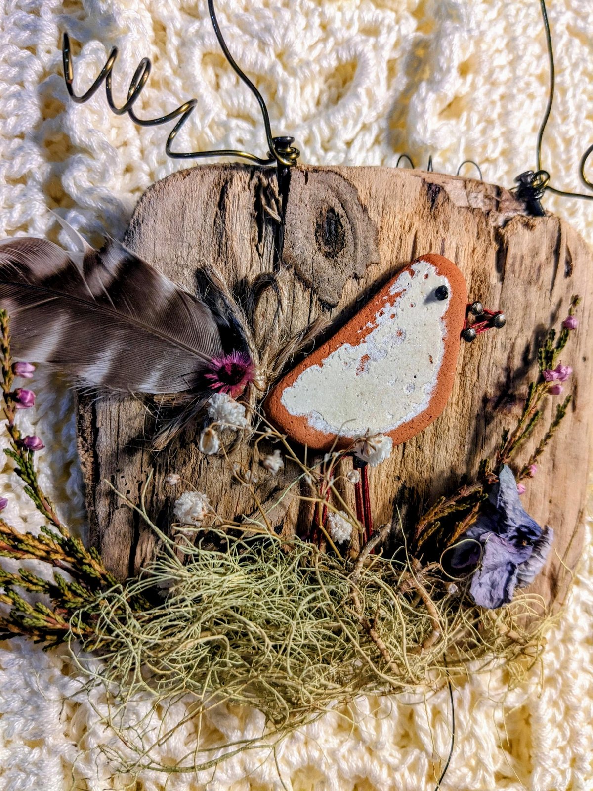 A terracotta robin made from beach finds mounted on weathered driftwood.