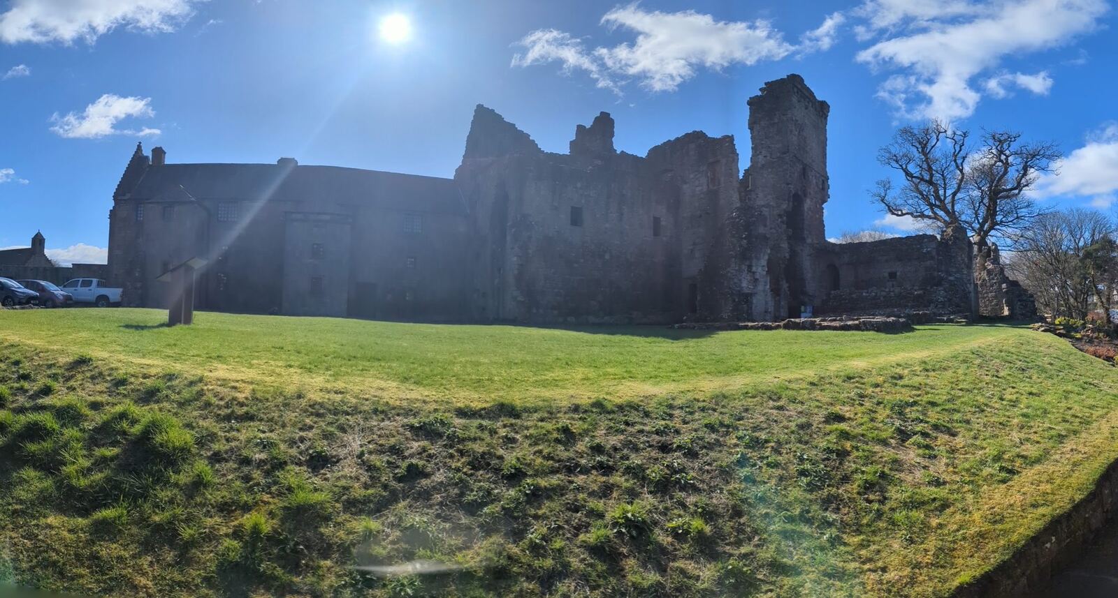 The ruined ranges and tower of Aberdour Castle on green lawn under a blue sky.