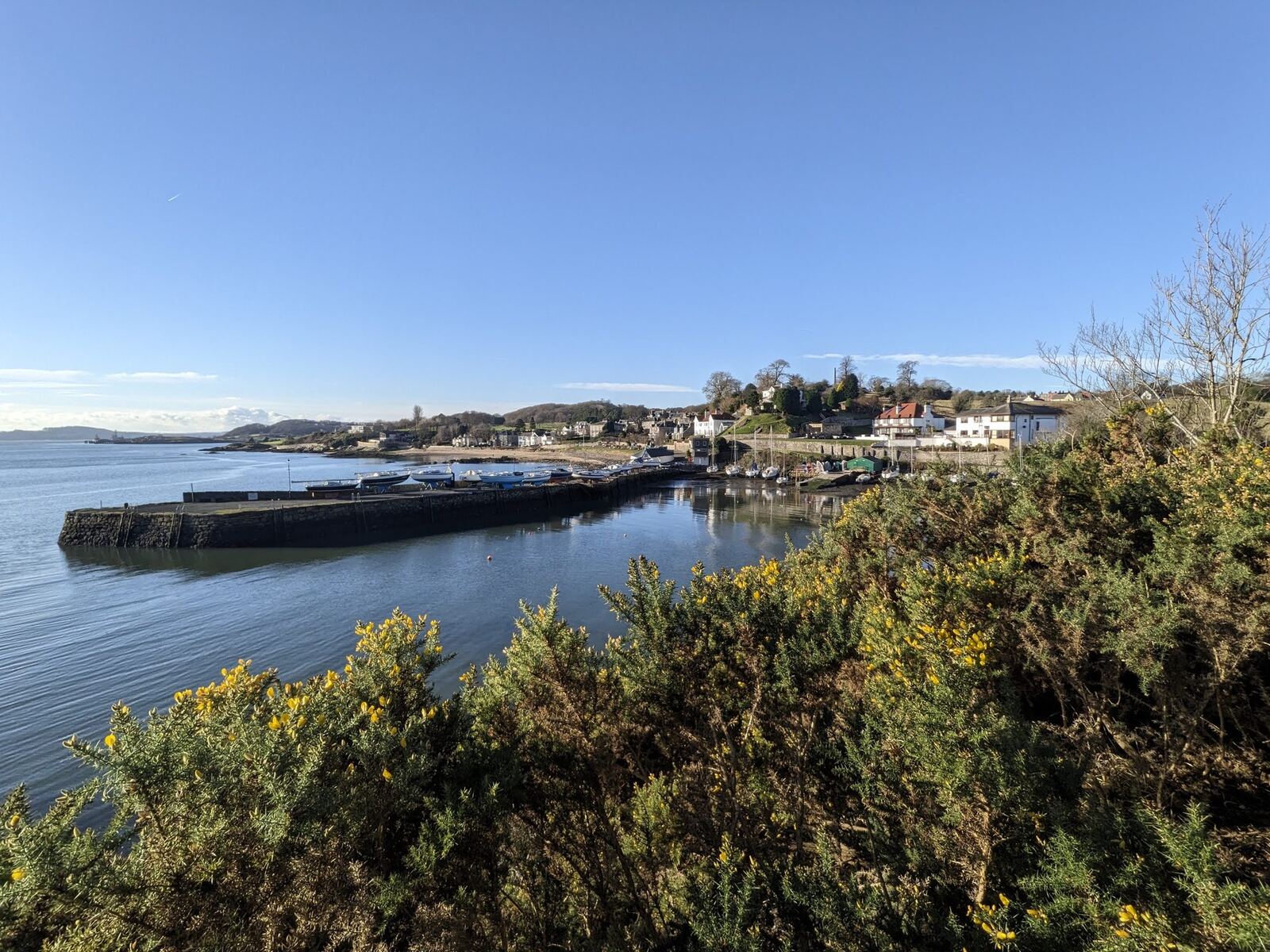 Aberdour village and its harbour across the bay on the Firth of Forth, blue sky.