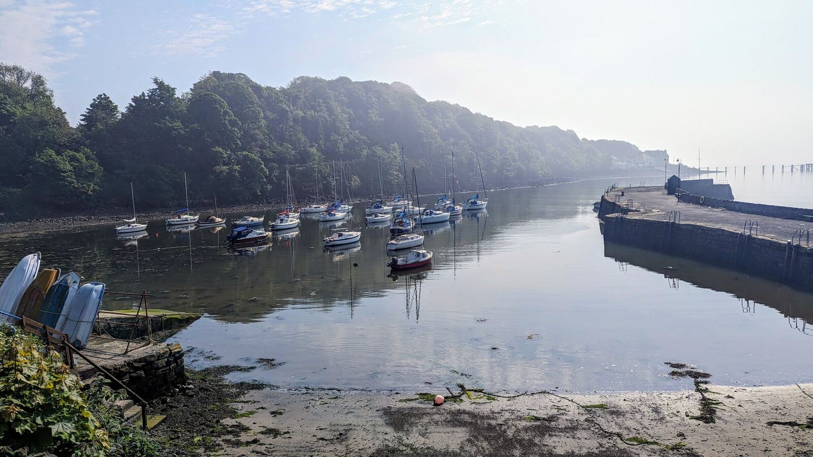 Aberdour harbour on a misty, still morning, boats reflected in calm water.