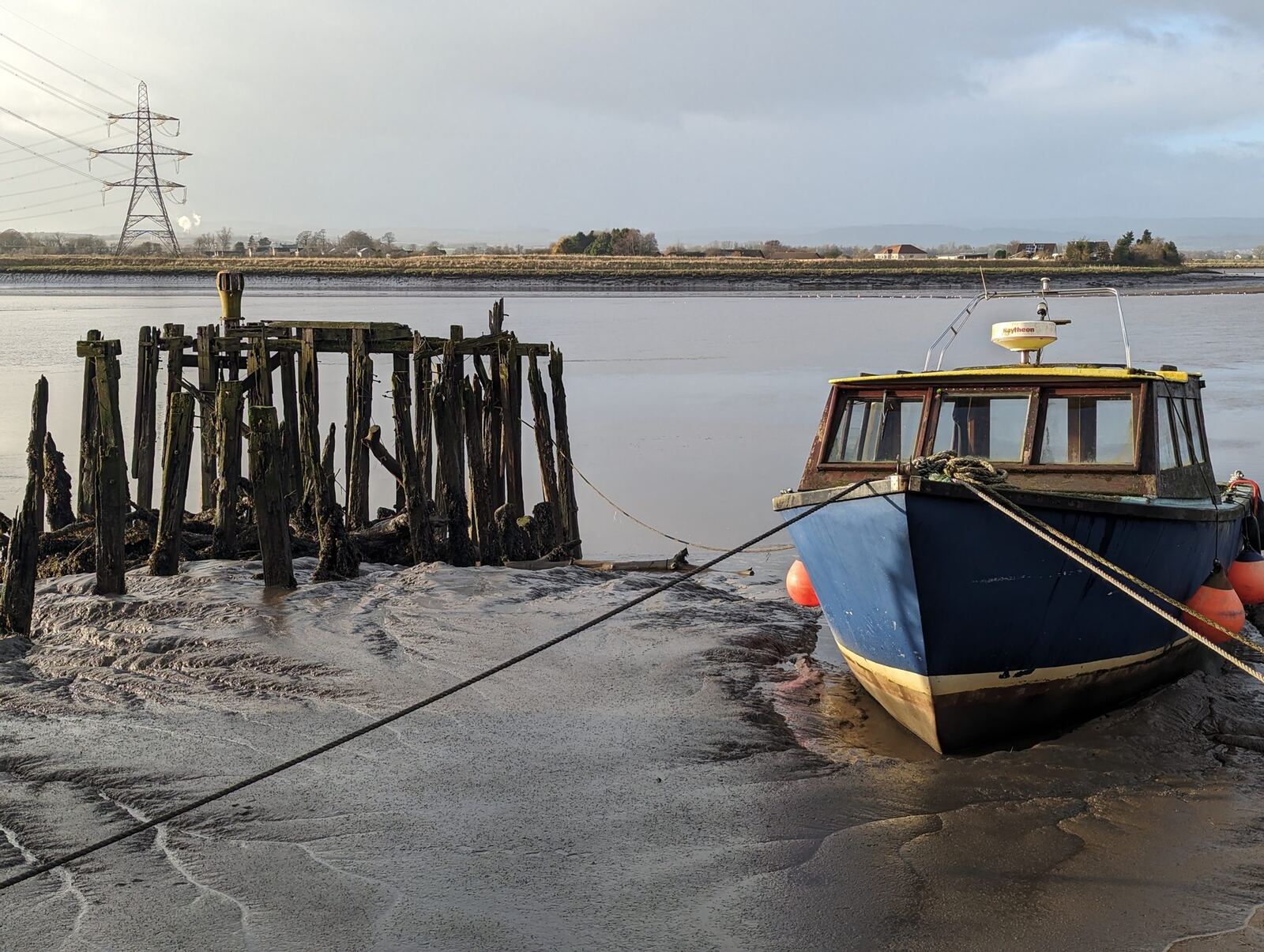 A small boat resting on the mud at low tide among old pilings on the Forth at Alloa.