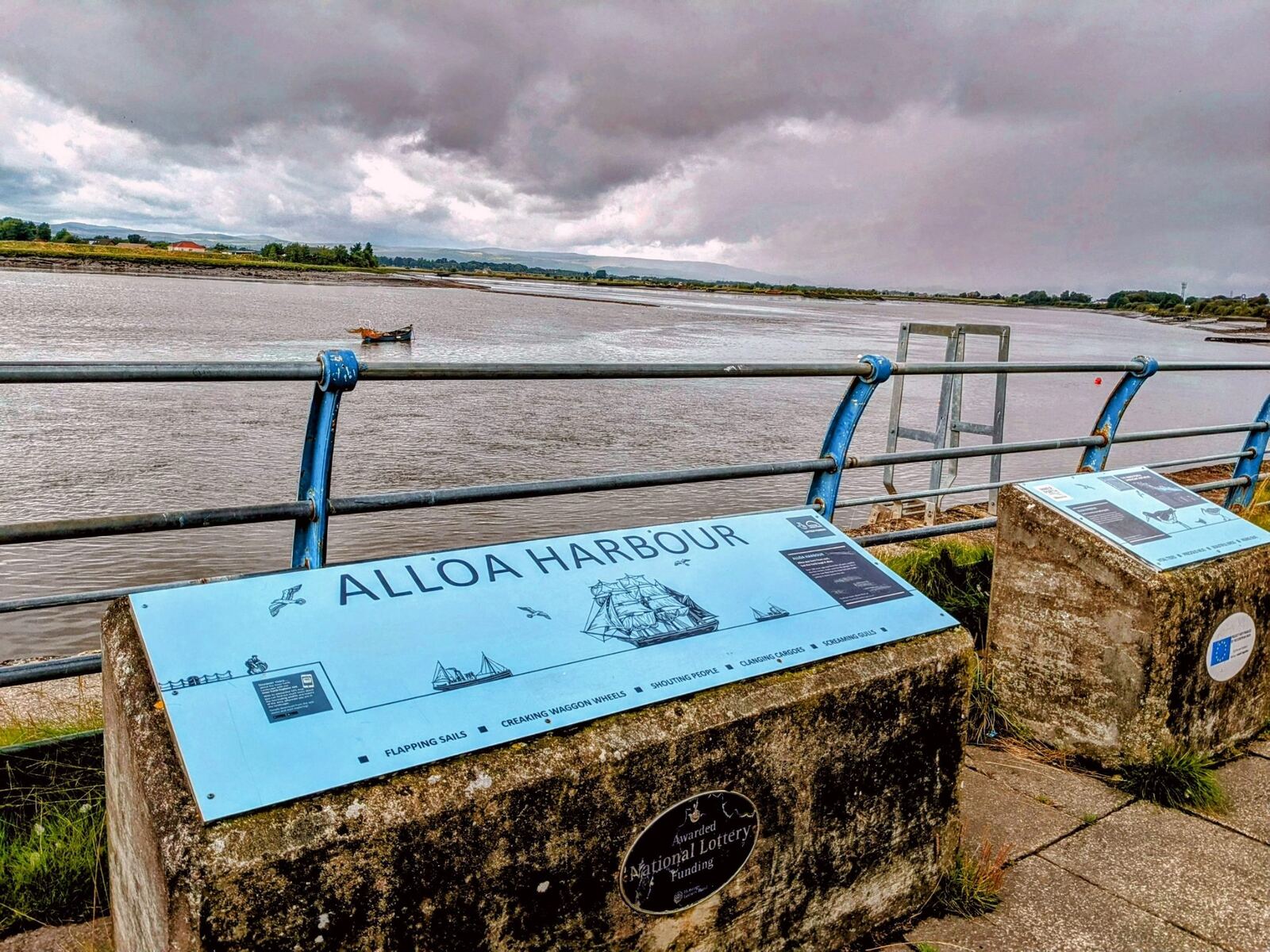 An 'Alloa Harbour' interpretation board beside the Firth of Forth, the wide estuary behind.