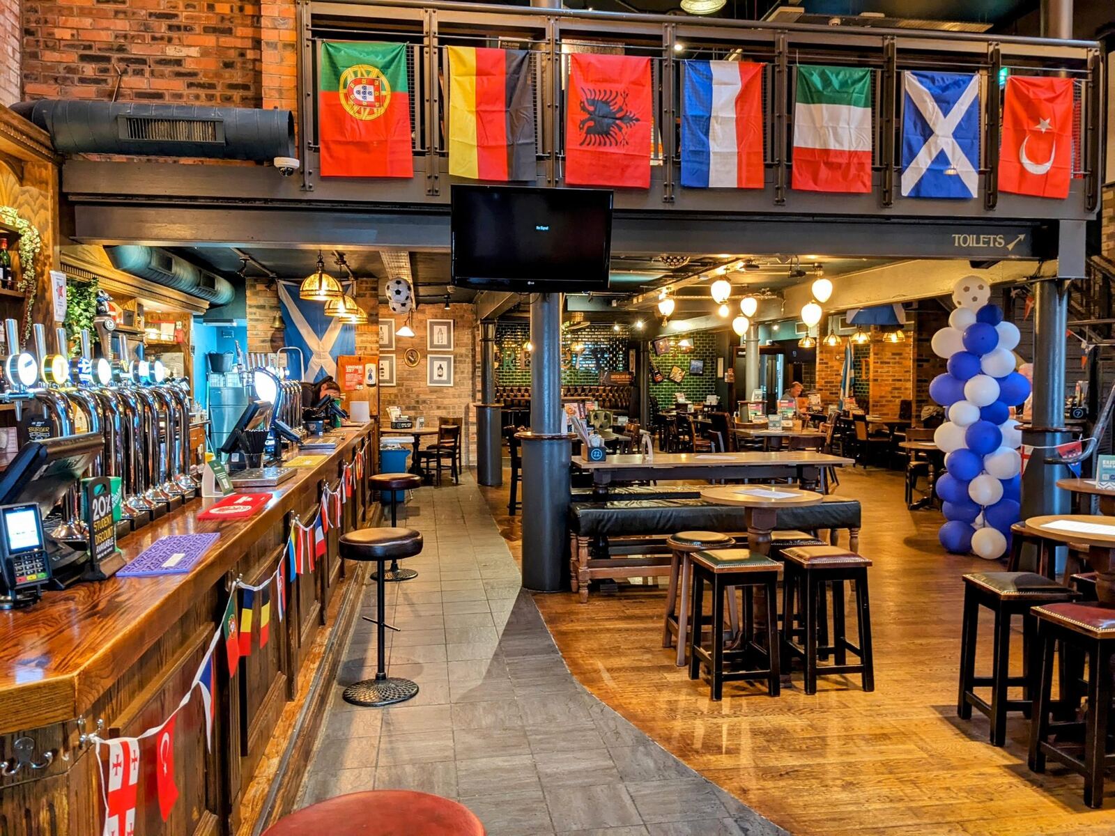 The warm interior of a traditional Alloa pub with flags and a busy bar.