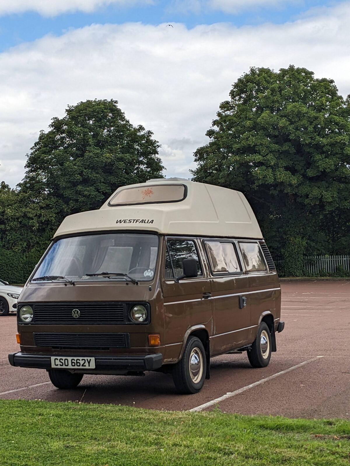 A classic left-hand-drive VW T25 Original Westfalia campervan parked by trees in Alloa.