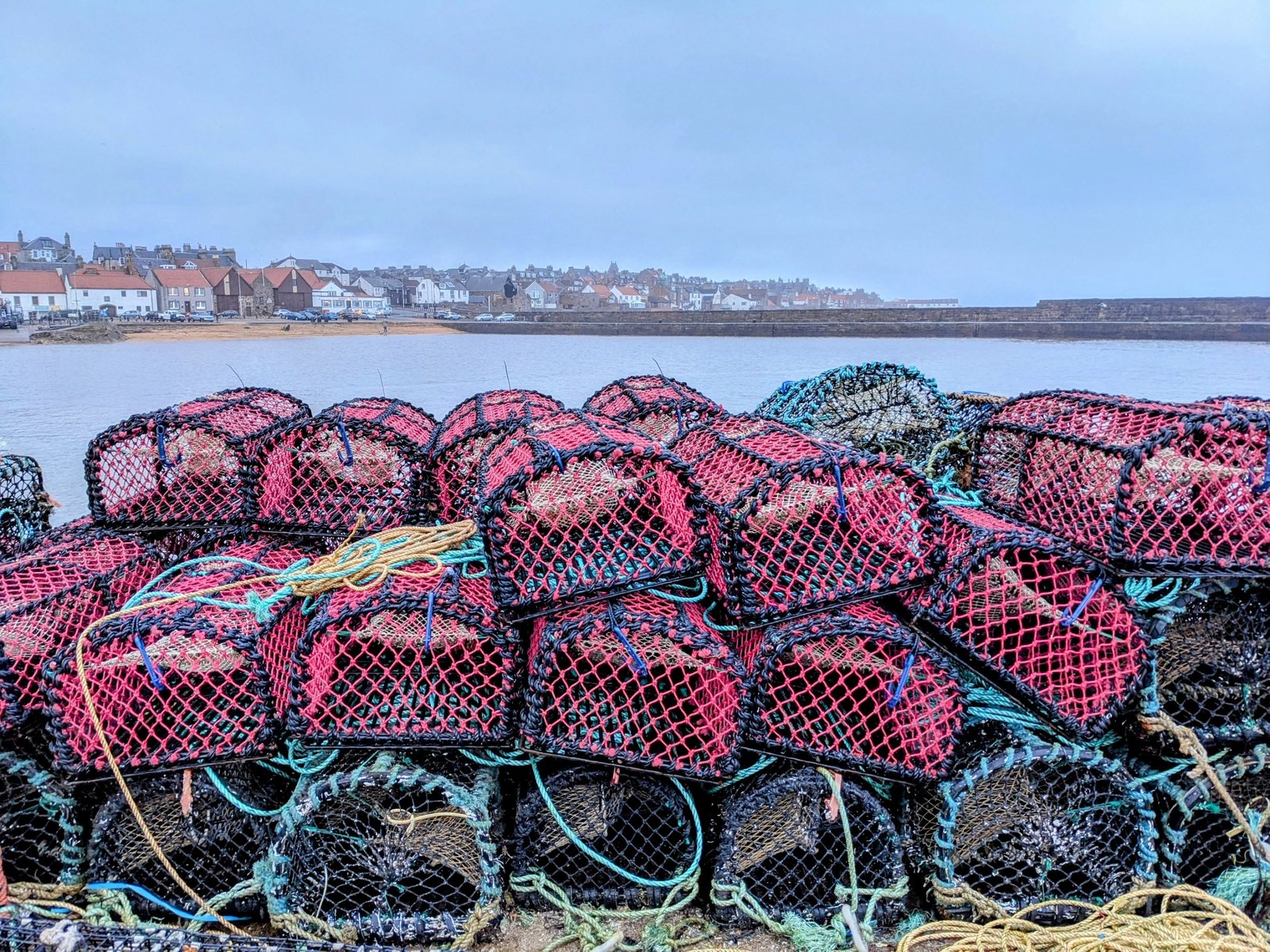 Creels stacked high on the quay at Anstruther, village behind.