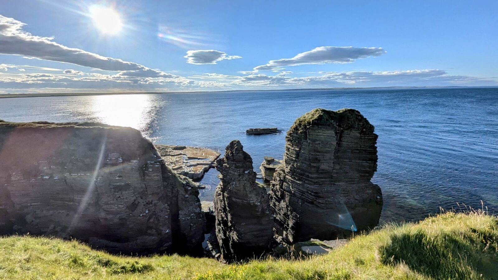 Layered flagstone sea stacks and cliffs at Noss Head near Castle Sinclair Girnigoe, blue sea and low sun.