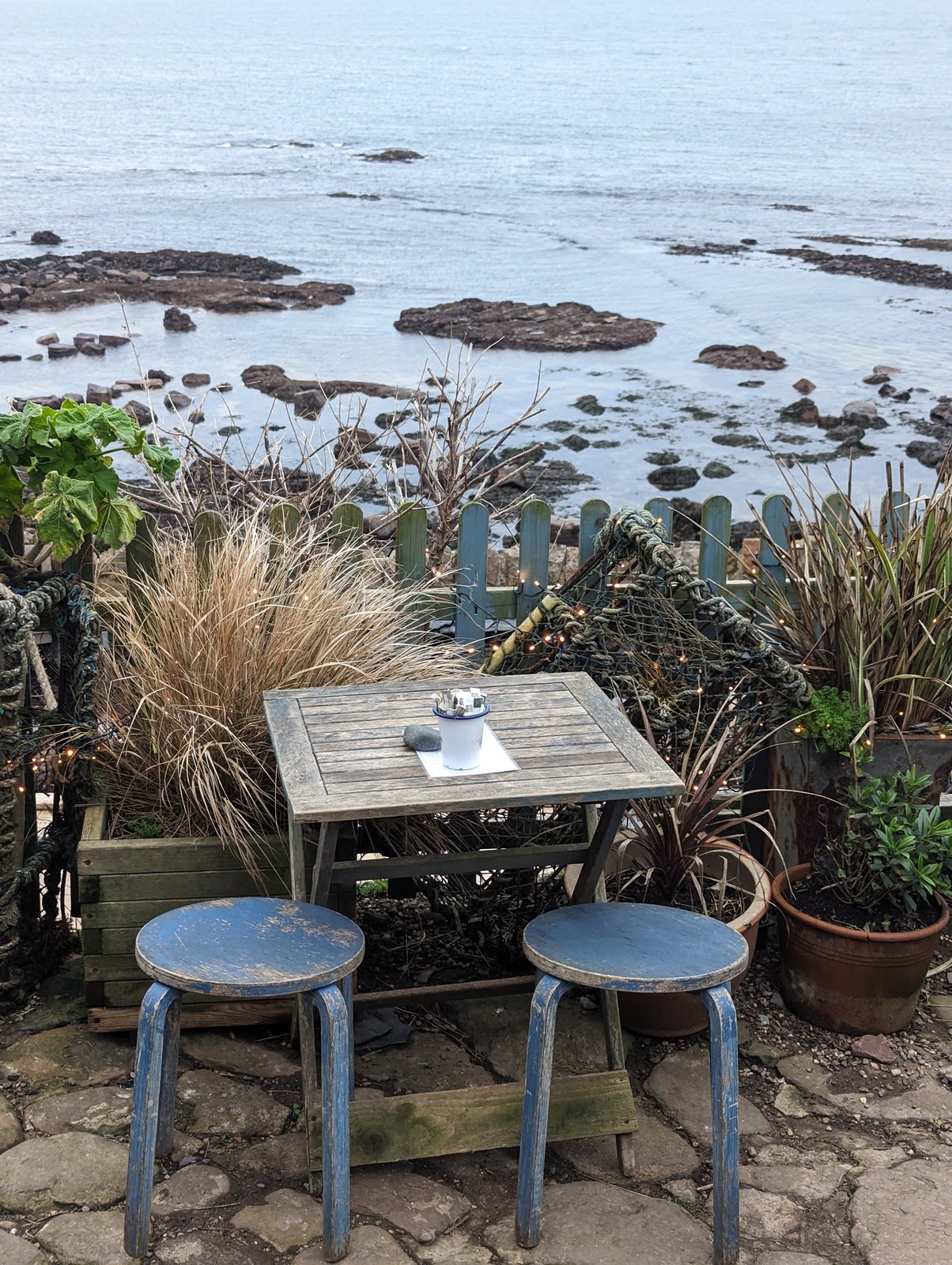 Tables on the terrace of the Crail Harbour Gallery and Tearoom above the water.