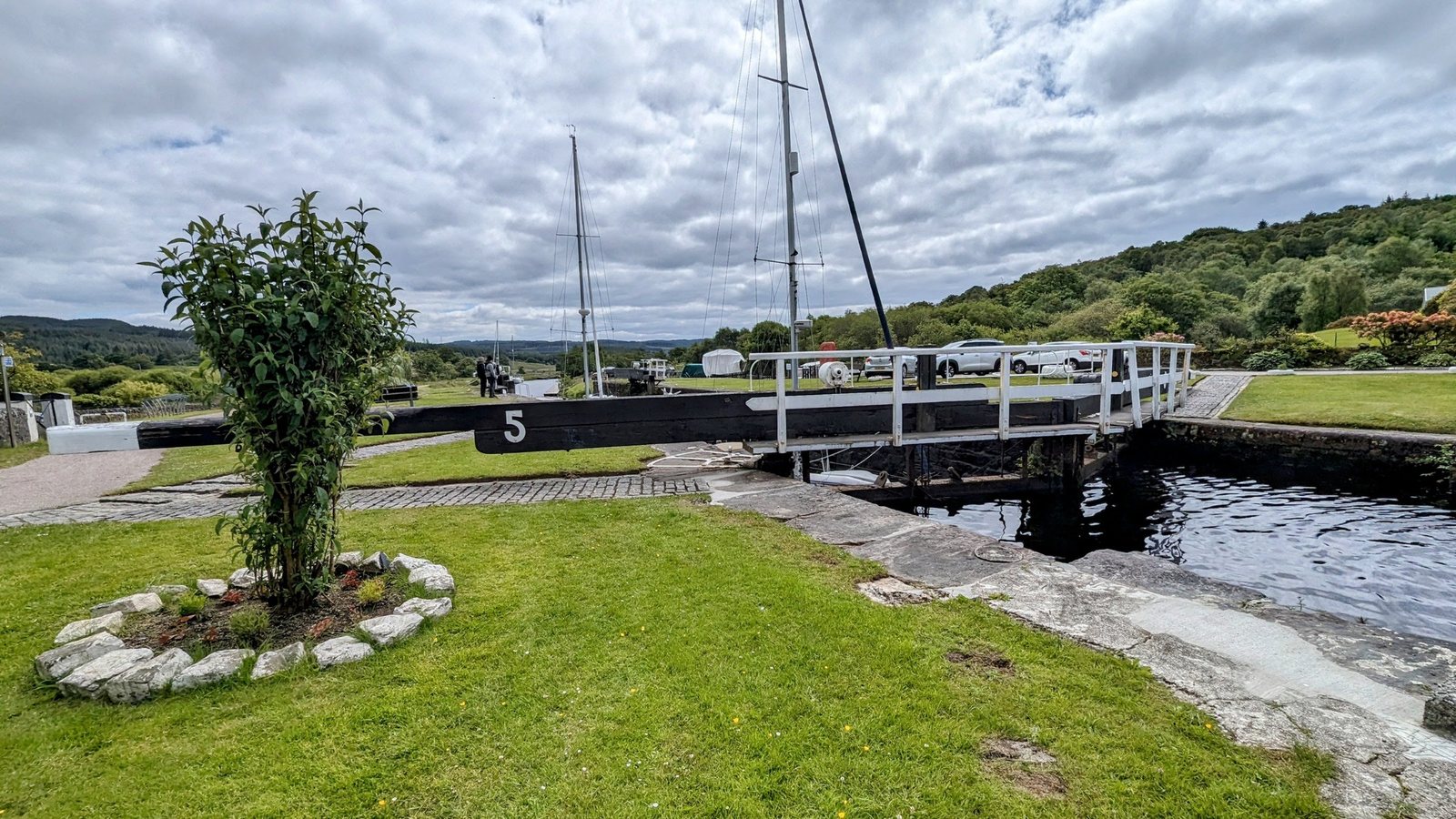 A small canal swing bridge beside a lock, with a canal-side lawn, on the Crinan Canal.