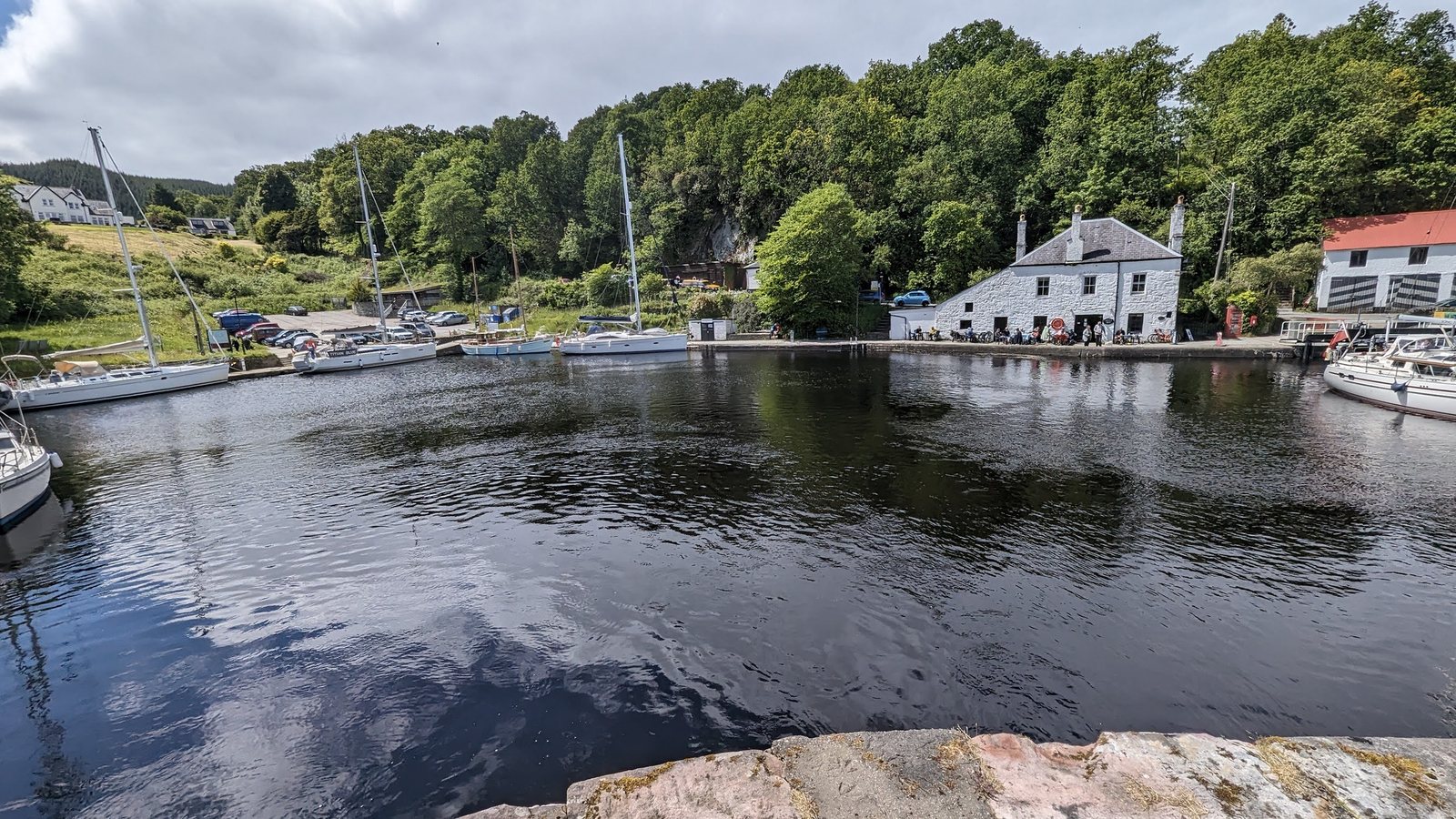 The still Crinan Canal basin with old white canal buildings and wooded hills behind.