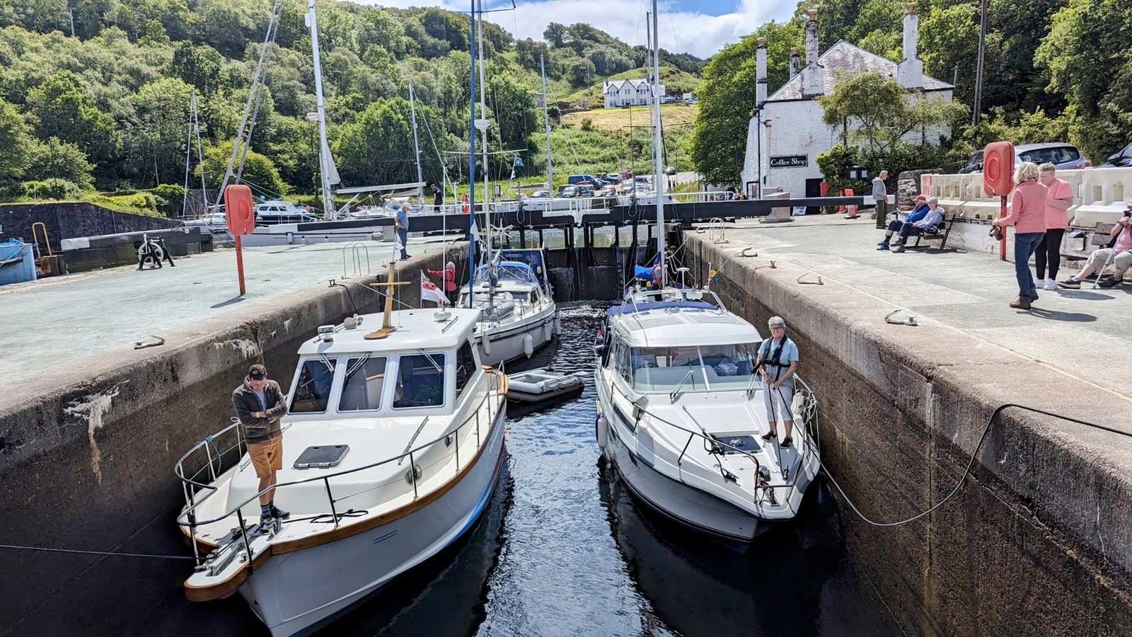 Two motor cruisers locking through the Crinan basin with people on the quayside.