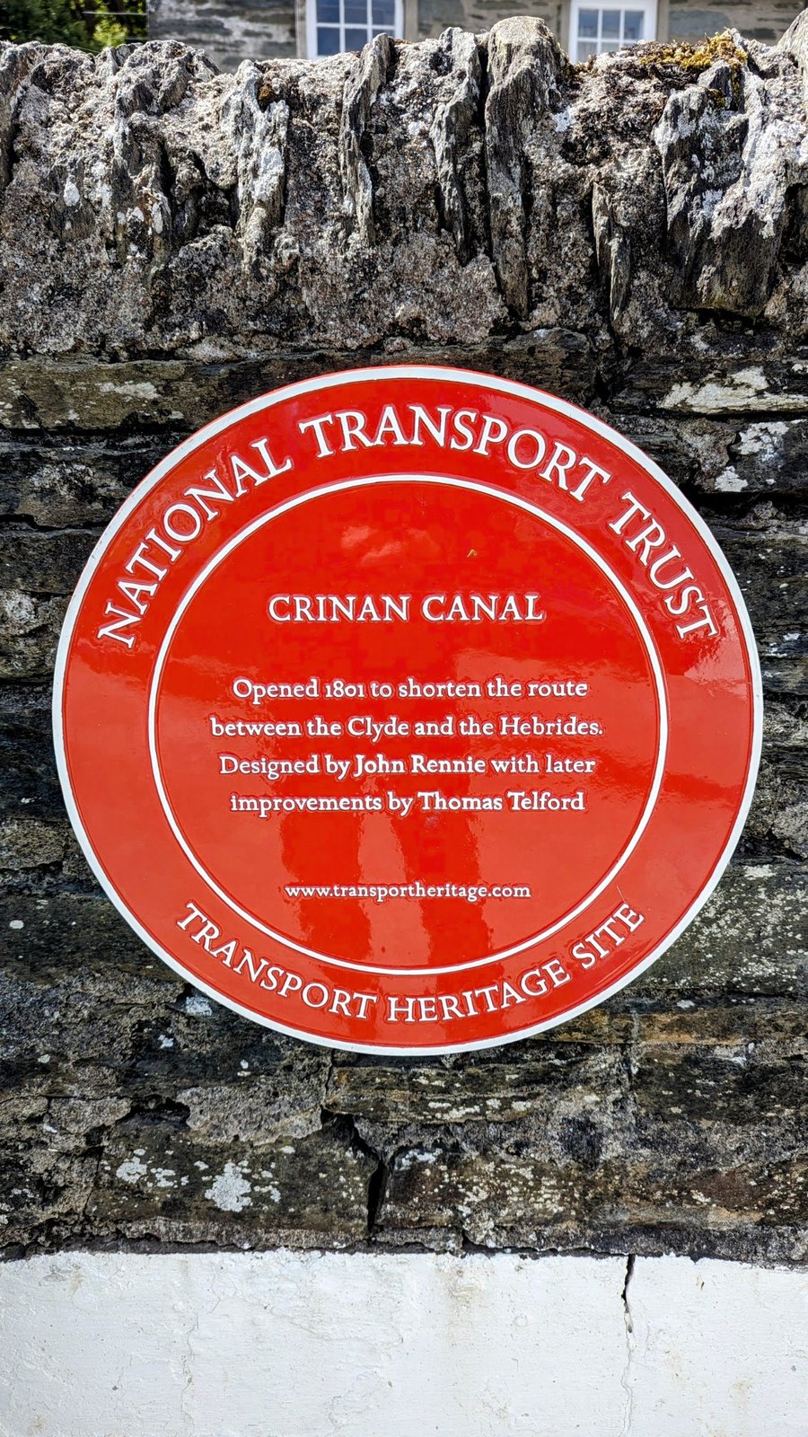 A red National Transport Trust heritage plaque for the Crinan Canal on a whitewashed wall.