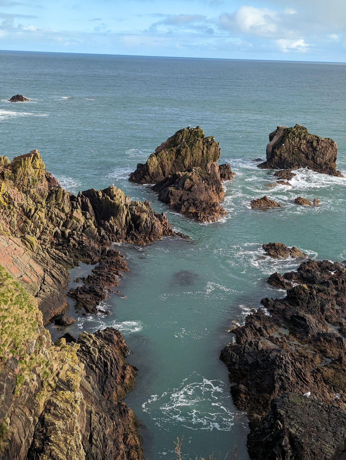 Red sea stacks and a turquoise cove below the cliffs at Slains, Cruden Bay.