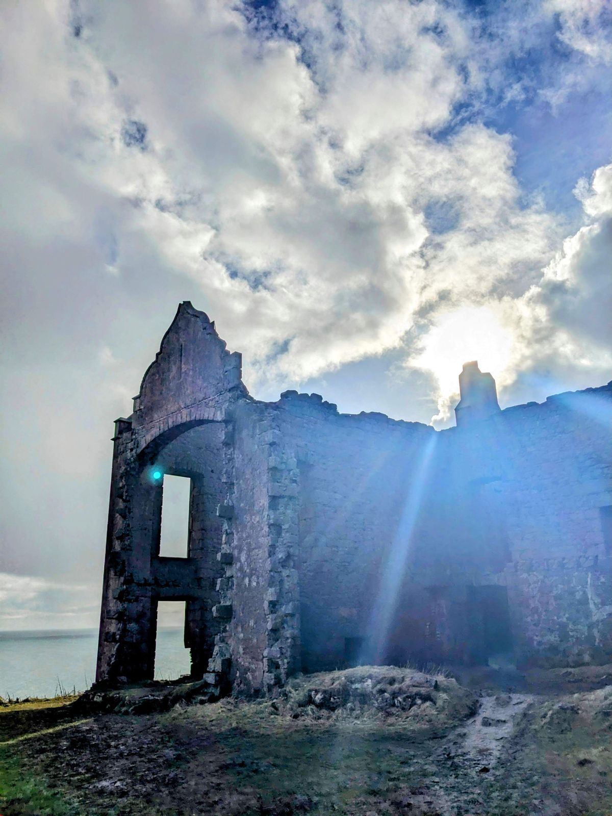 A gable of Slains Castle silhouetted against a burst of sun.