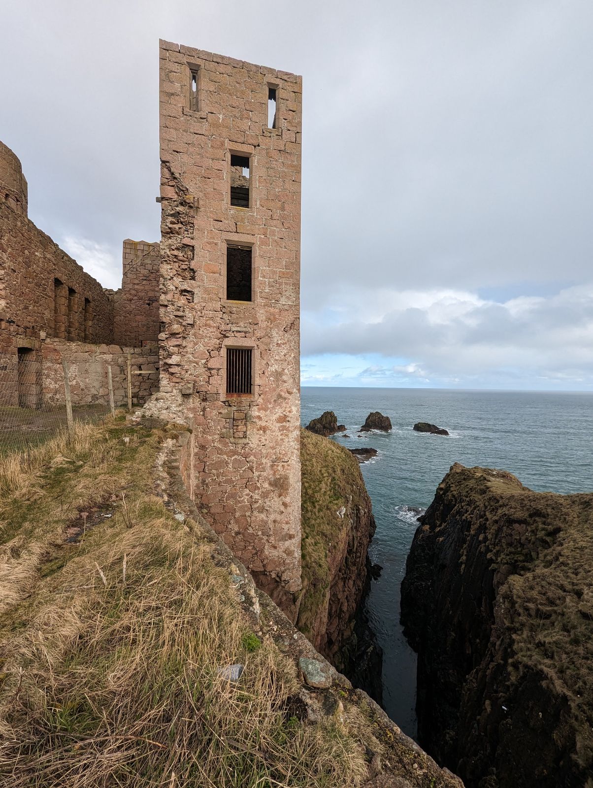 The tall red-stone tower of Slains Castle standing on the cliff edge.