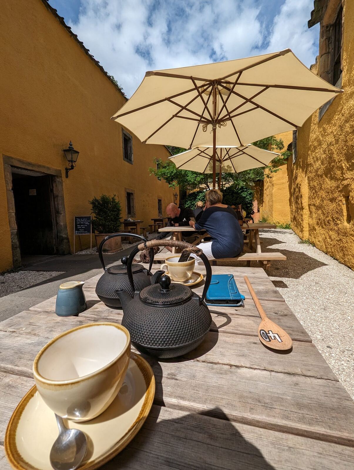 A sunny courtyard with a parasol and cast-iron teapots against ochre walls at a Culross café.