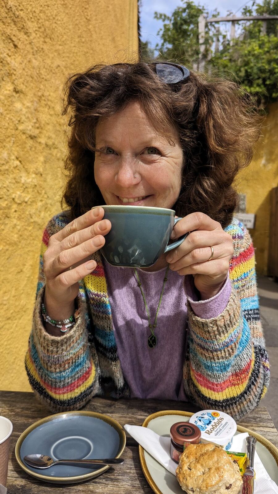 A person holding a mug of coffee at a Culross café table with a scone.