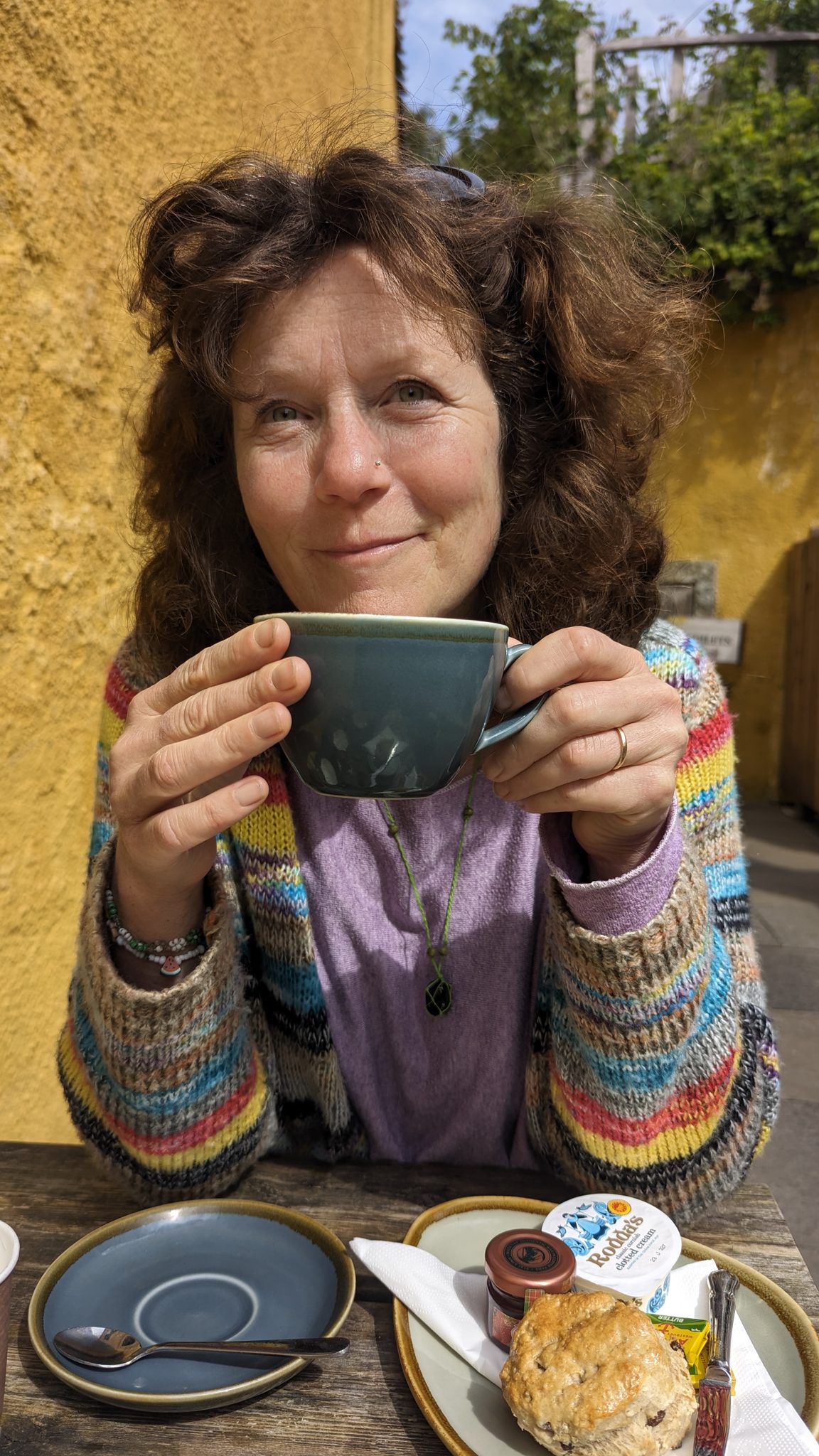 A visitor with a mug of tea against the ochre courtyard wall of a Culross café.