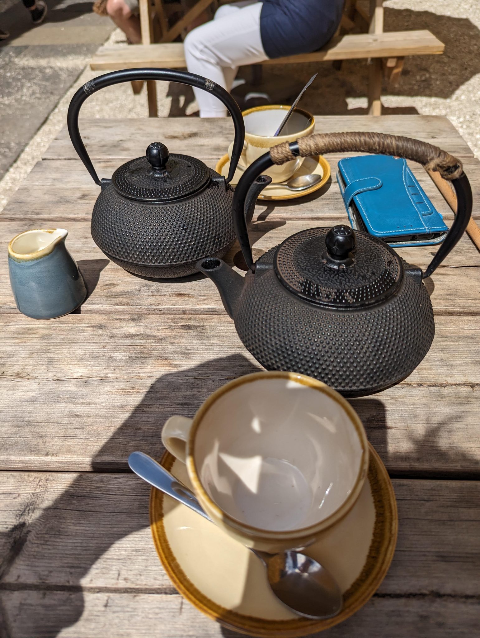 Cast-iron teapots and cups on a wooden table in the sunny ochre courtyard of a Culross café.