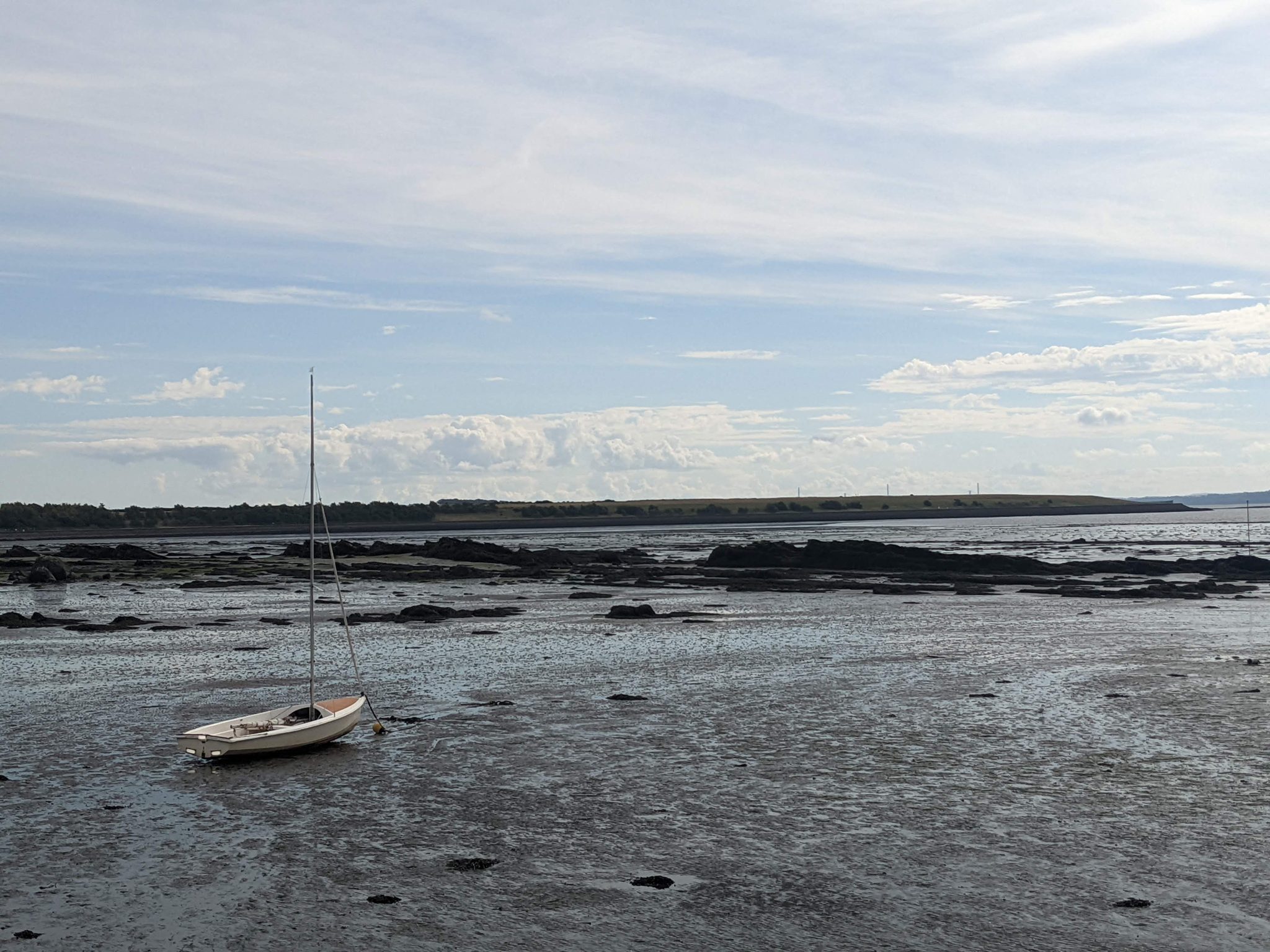 A small boat moored on the Firth of Forth at Culross at low tide, distant hills beyond.