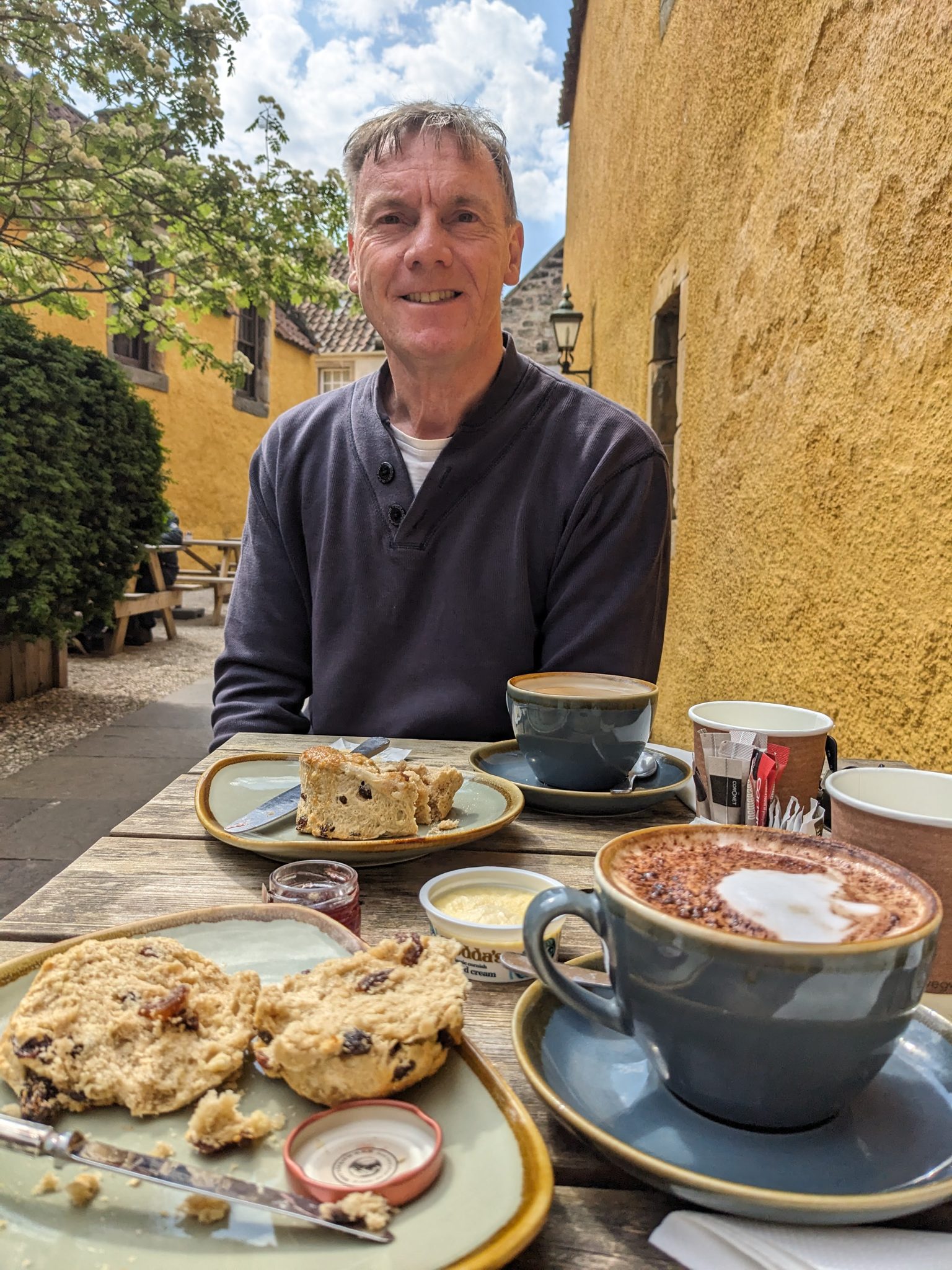 Kevin at a café table in the ochre courtyard garden at Culross with scones and coffee.