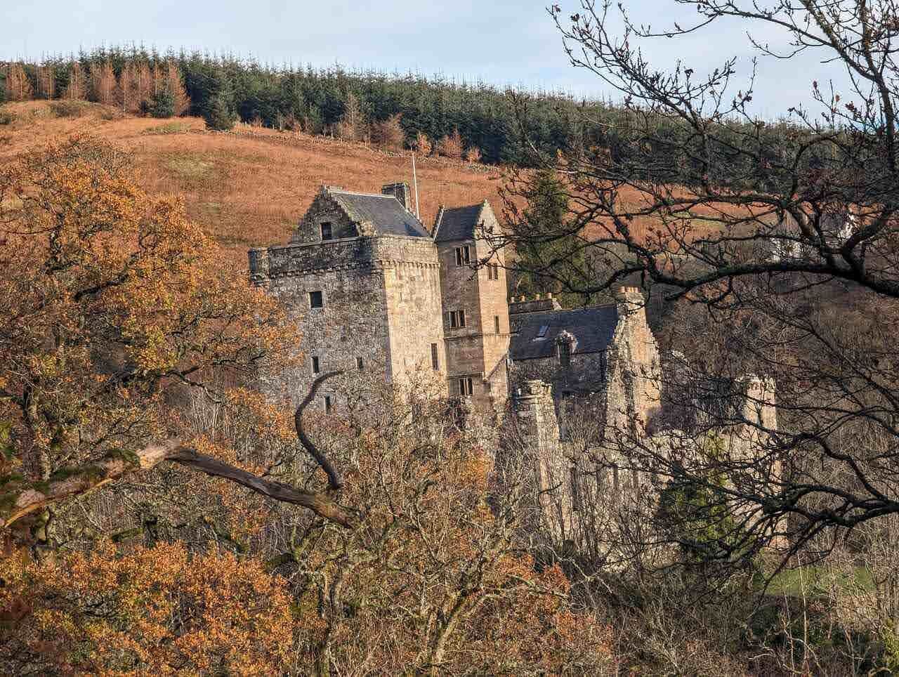 Castle Campbell across the autumn bracken of Dollar Glen, forested hills behind.