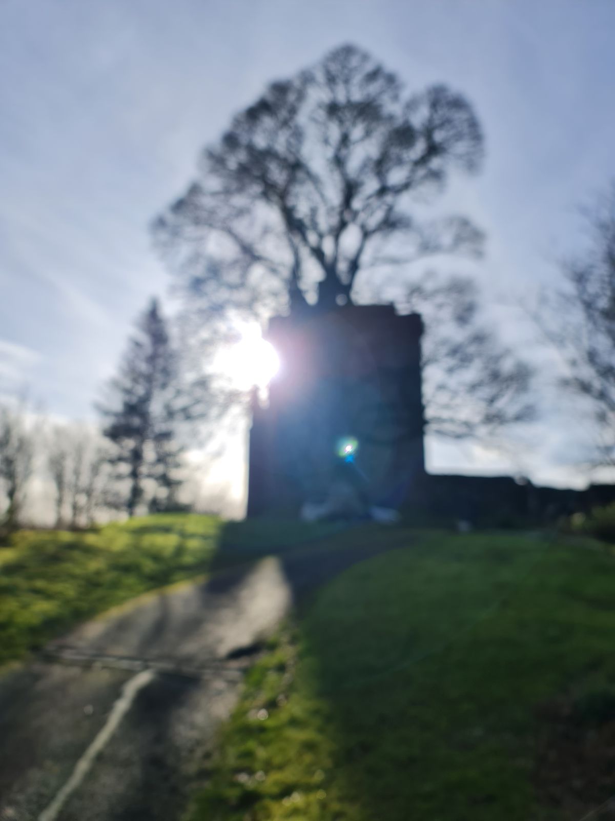 The tower of Castle Campbell silhouetted against a low sun burning through a bare tree
