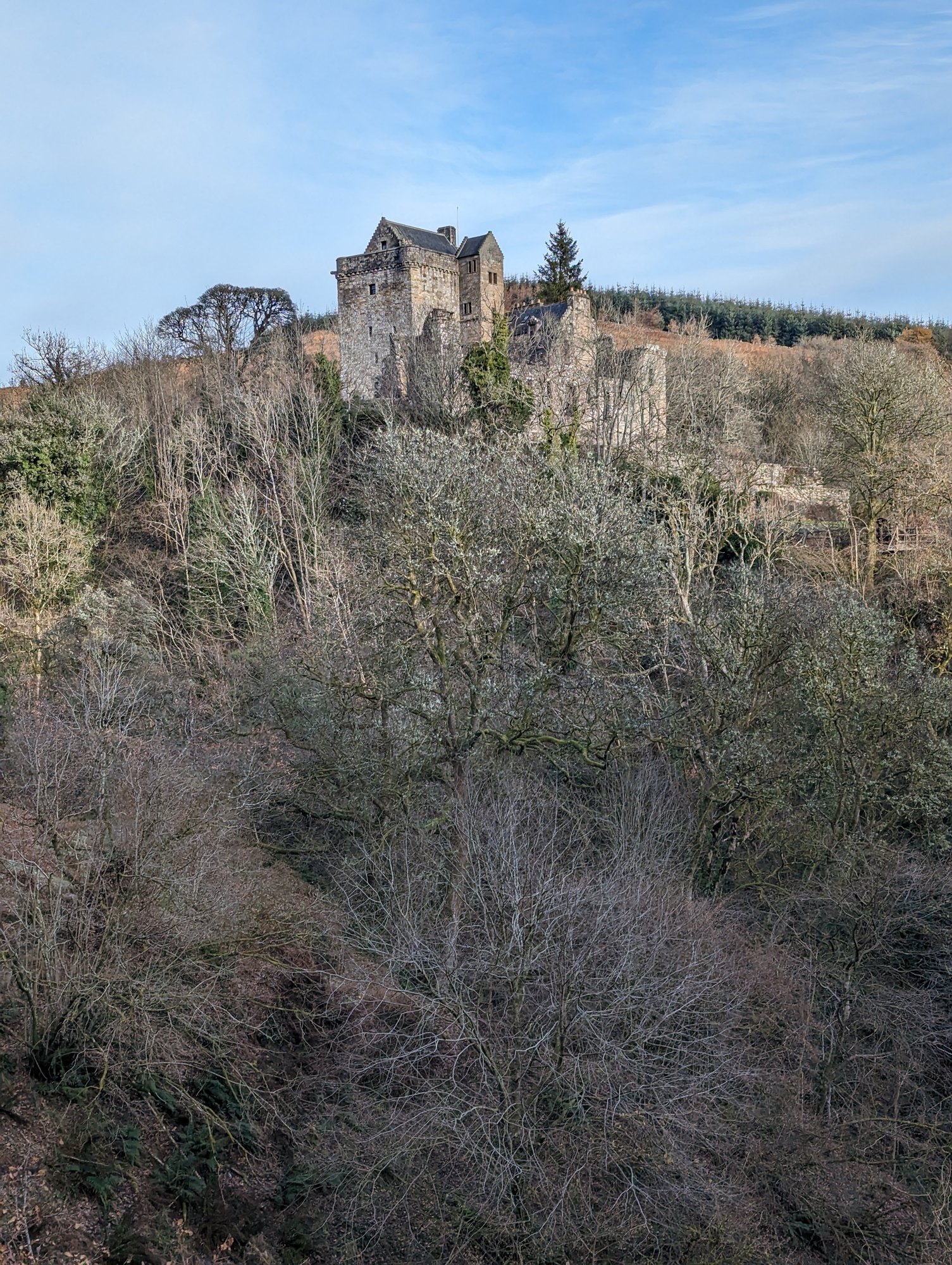 Castle Campbell standing on its rocky crag above bare winter woodland, under a blue sky