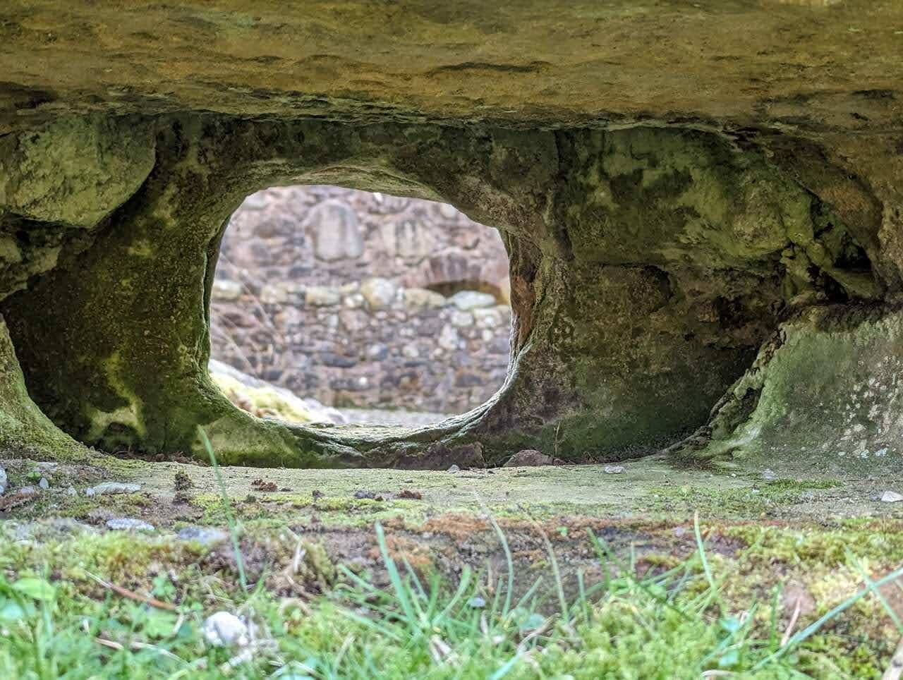 A natural rock arch in Dollar Glen framing the ruins of Castle Campbell beyond.