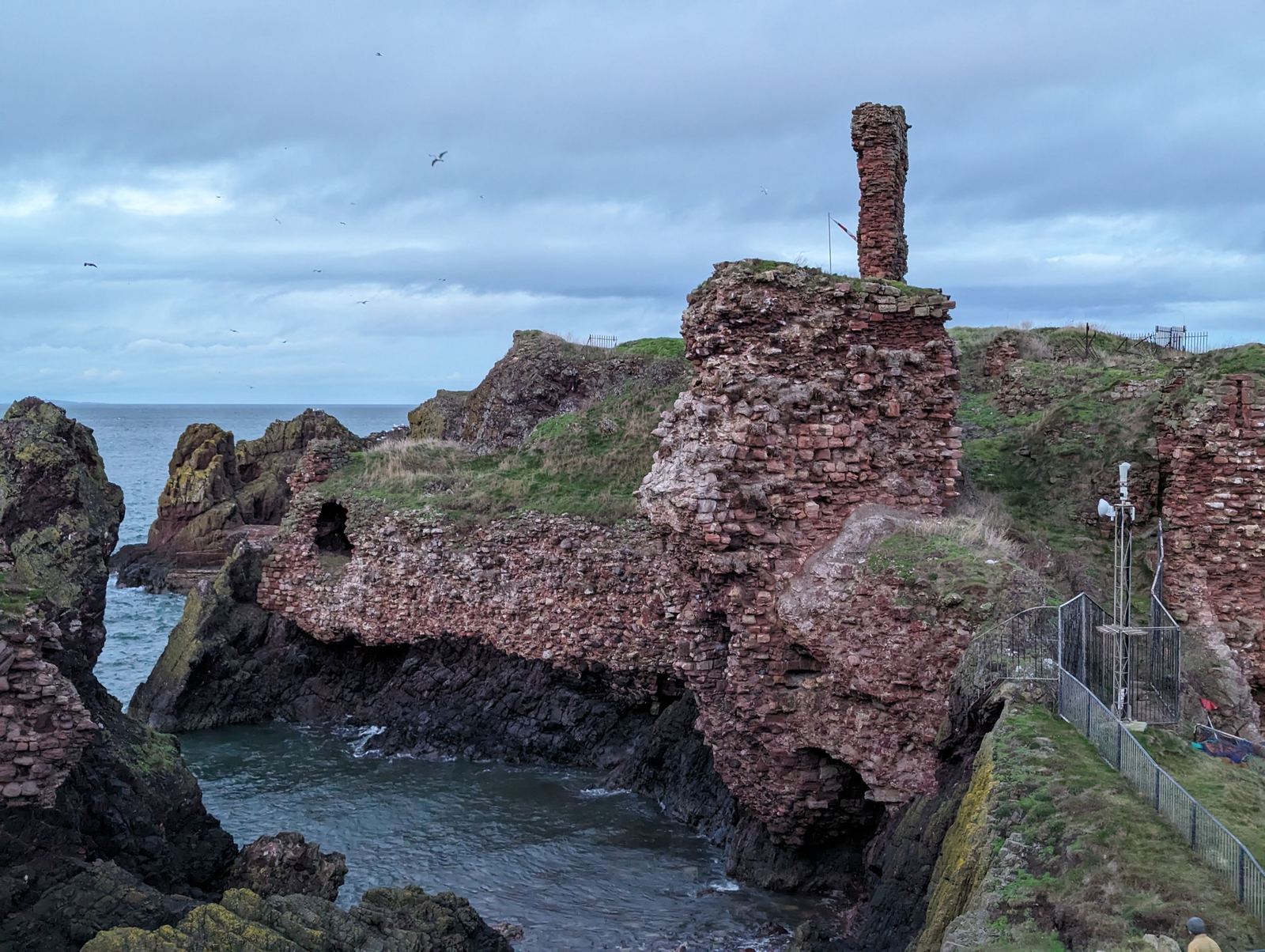 A natural rock arch beneath the red ruins of Dunbar Castle.