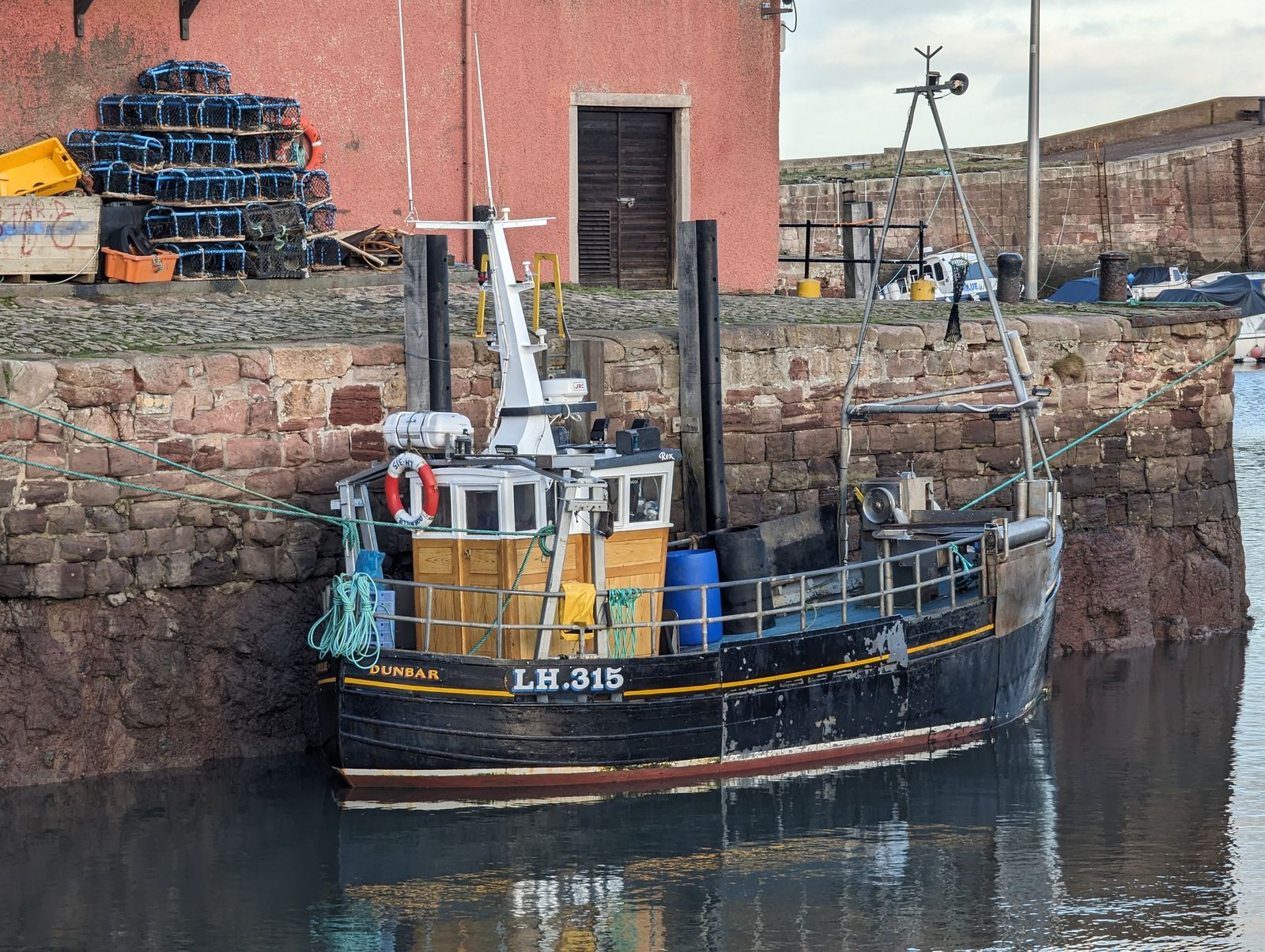 Fishing boats moored in Dunbar's Victoria Harbour, red sandstone buildings around it.