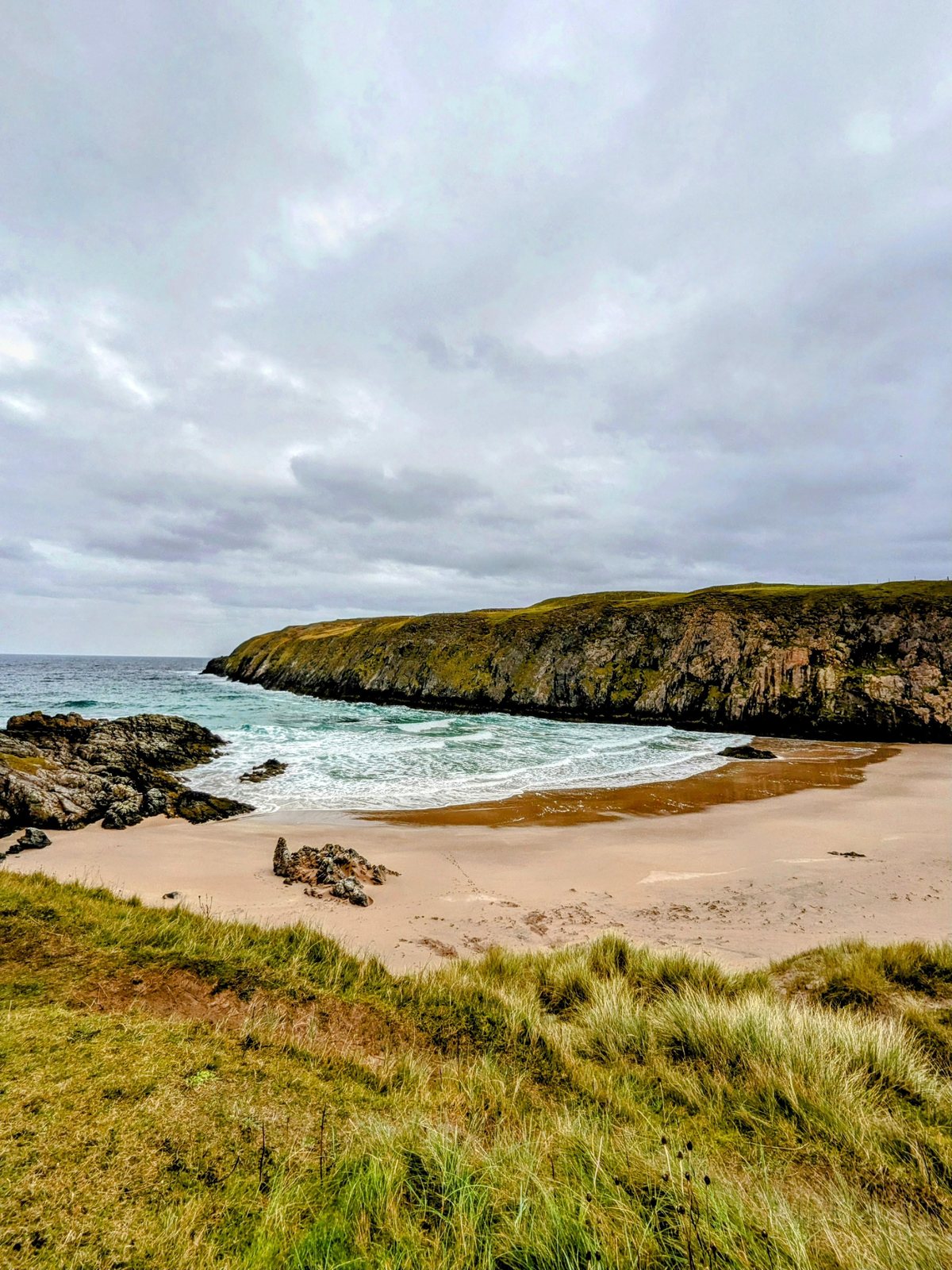 A person walking a beach cove at Durness.