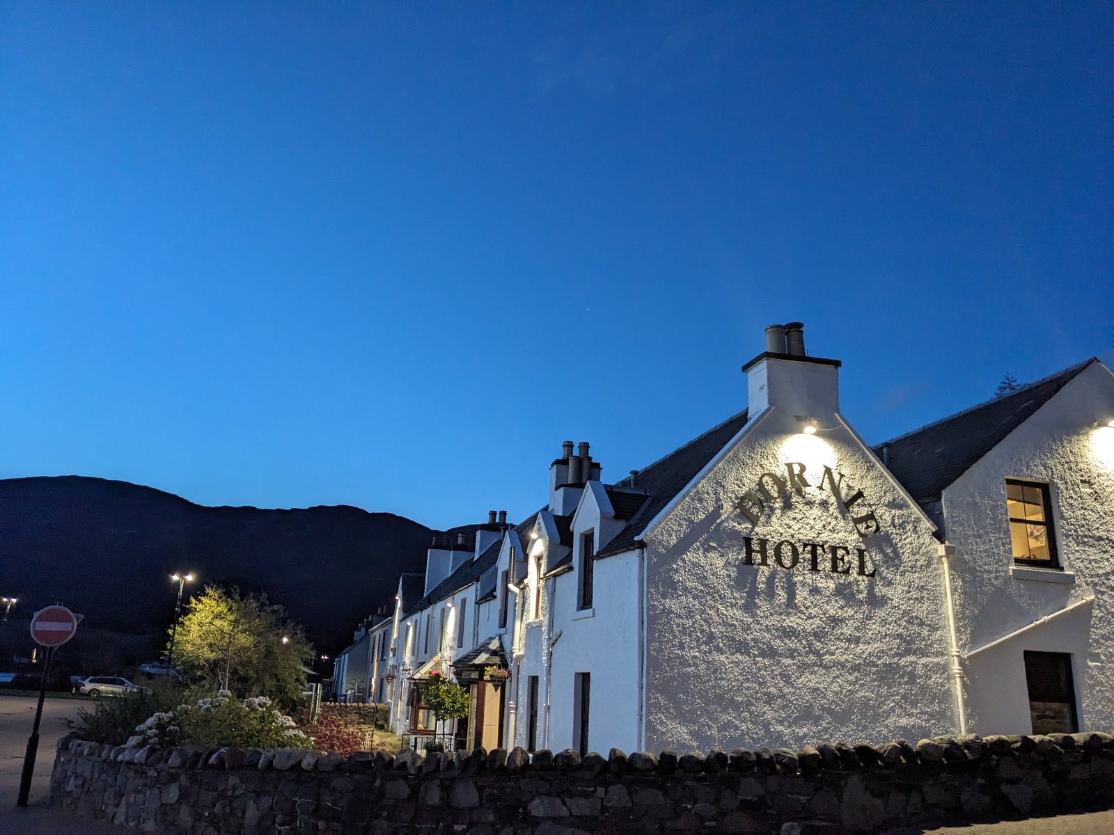 A white-walled hotel on the main street at Dornie, lit up at dusk under a deep blue sky