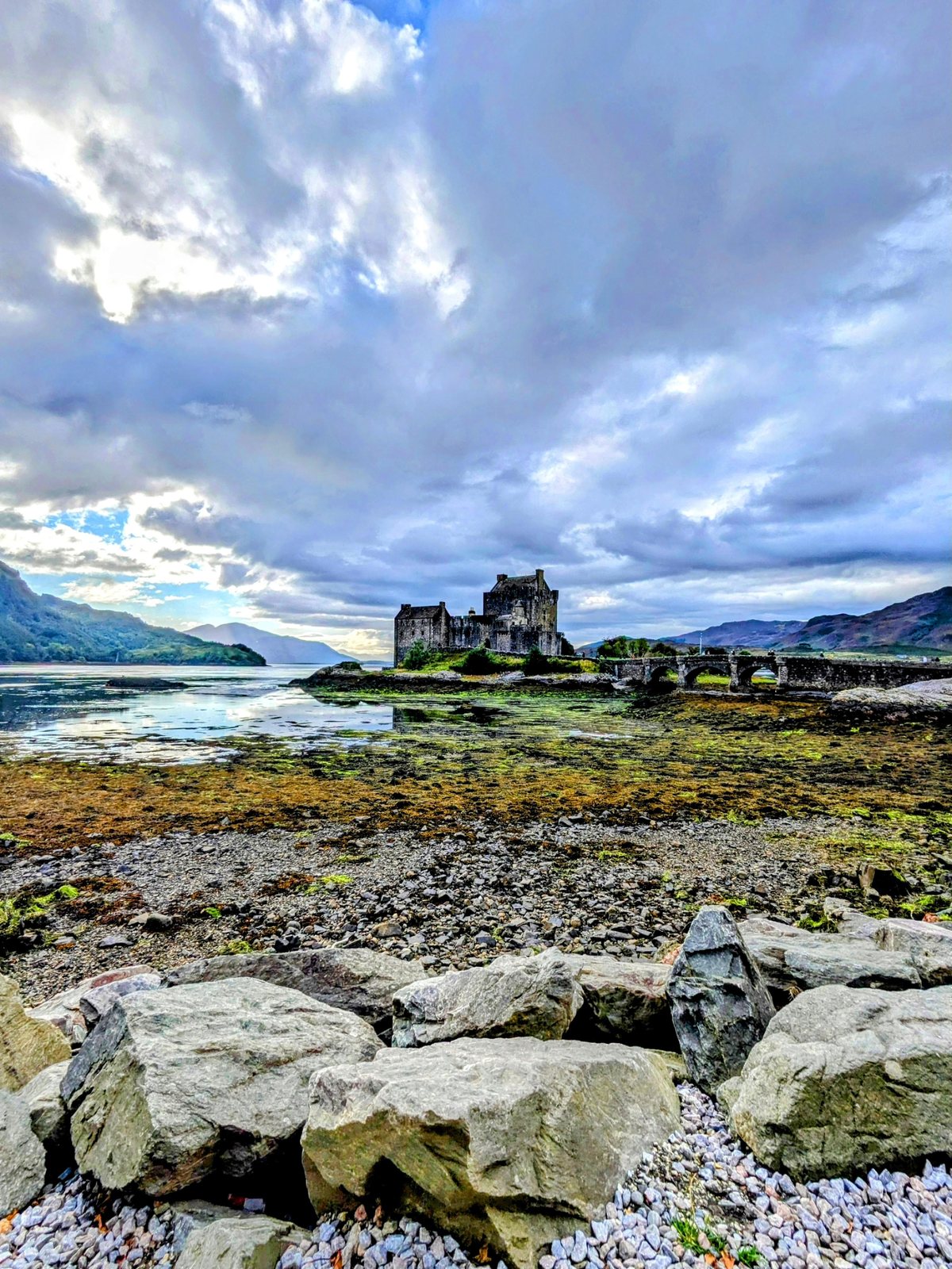 Eilean Donan Castle across the water at low tide, seaweed-covered foreshore and big pale boulders in the foreground