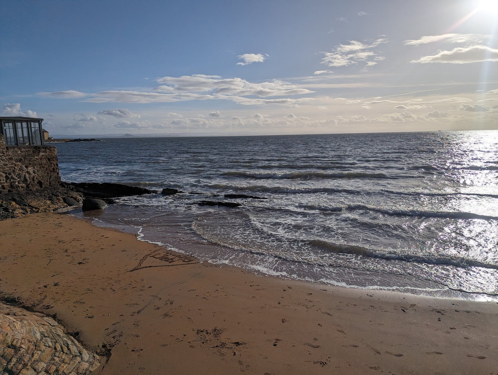 A small sandy beach beside the old stone harbour granary at Elie, the Forth beyond in low winter sun.
