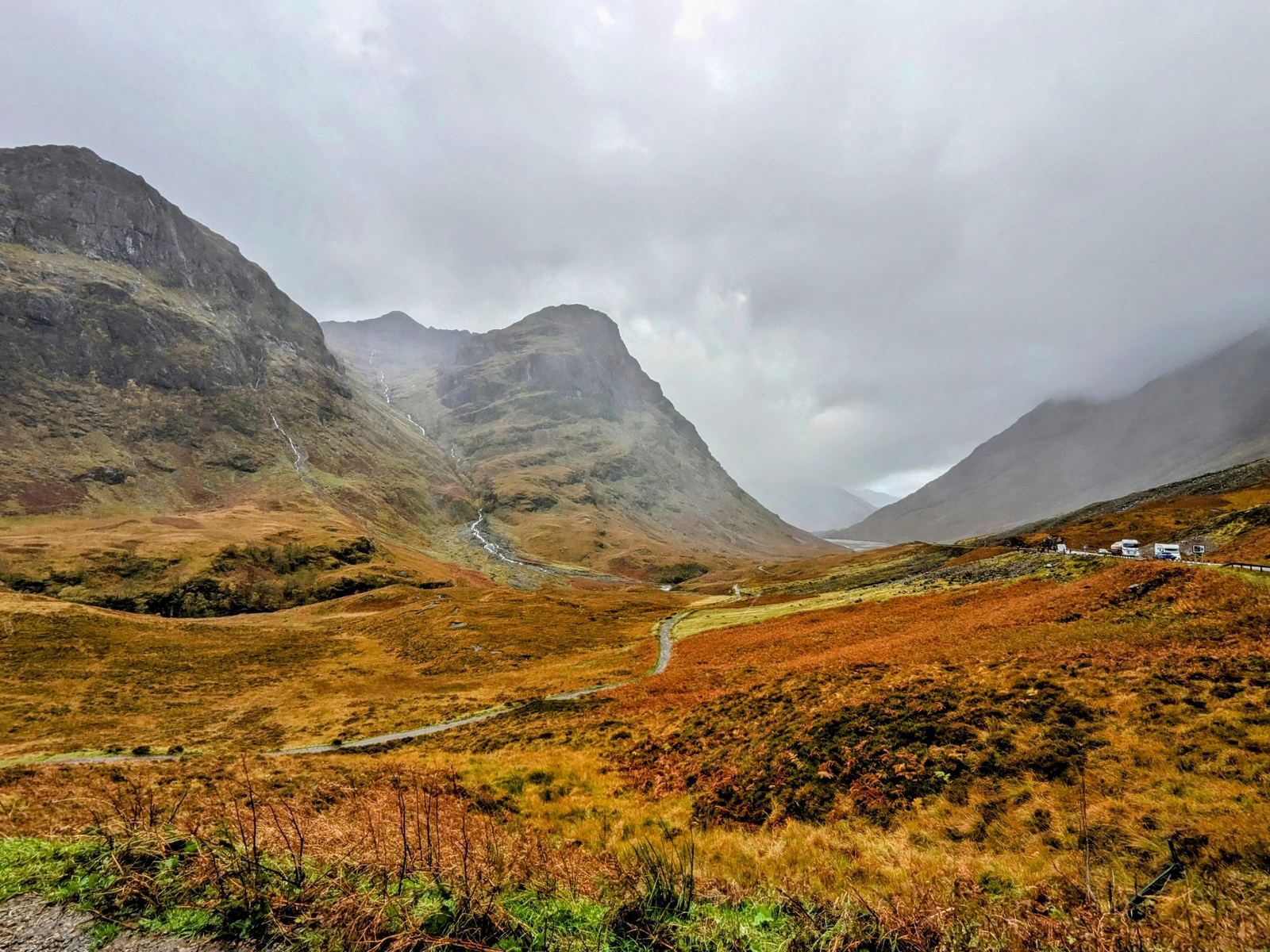 Misty, cloud-wreathed mountain peaks above a deep autumn glen on the road into Glen Coe.