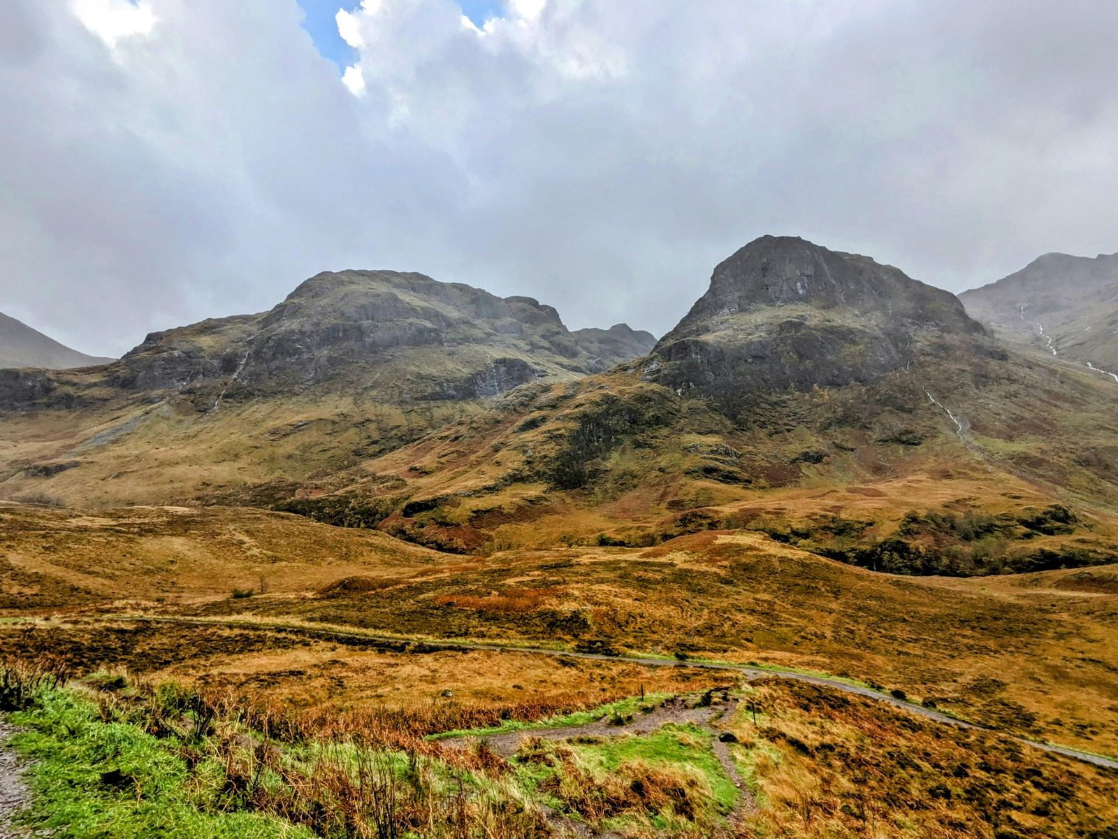 Rugged mountains rising steeply on either side of Glen Coe in autumn, moorland in the foreground.