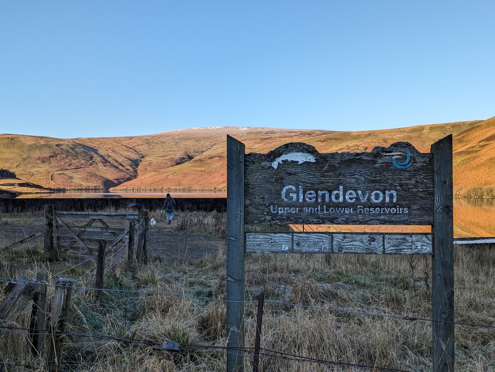 A wooden sign reading Glendevon Upper and Lower Reservoirs, with the hills behind.