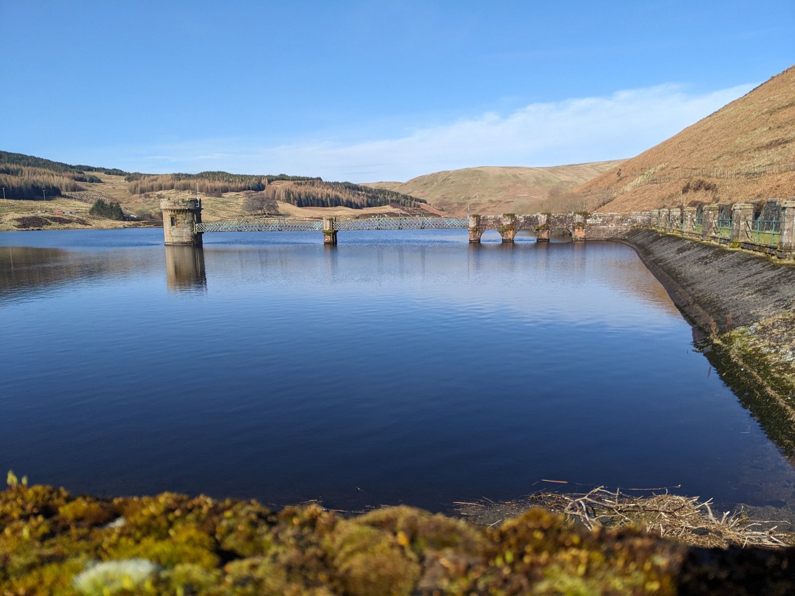 A reservoir valve tower reflected in still water at Glendevon, with a low winter sun.