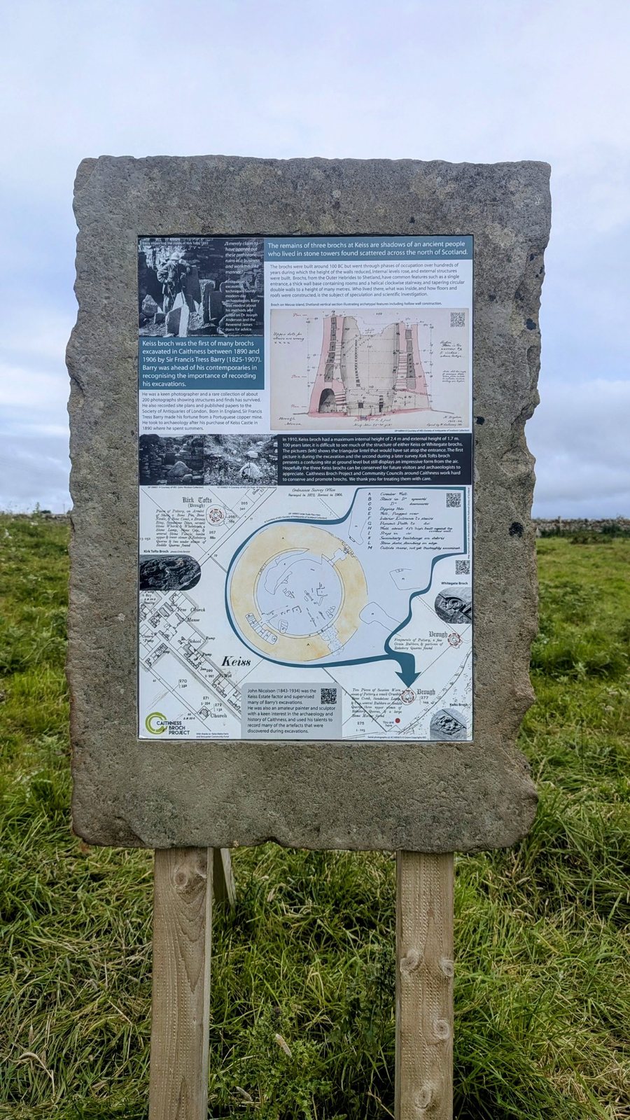 A Caithness Broch Project interpretation board mounted on a rough stone slab in a grassy field at Keiss, showing historic plans and photos of the Keiss brochs.