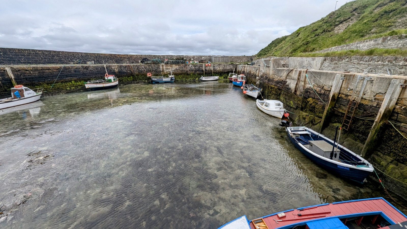 The stone slipway and harbour wall at Keiss at low tide, seaweed-covered rock exposed, a van parked in the distance.