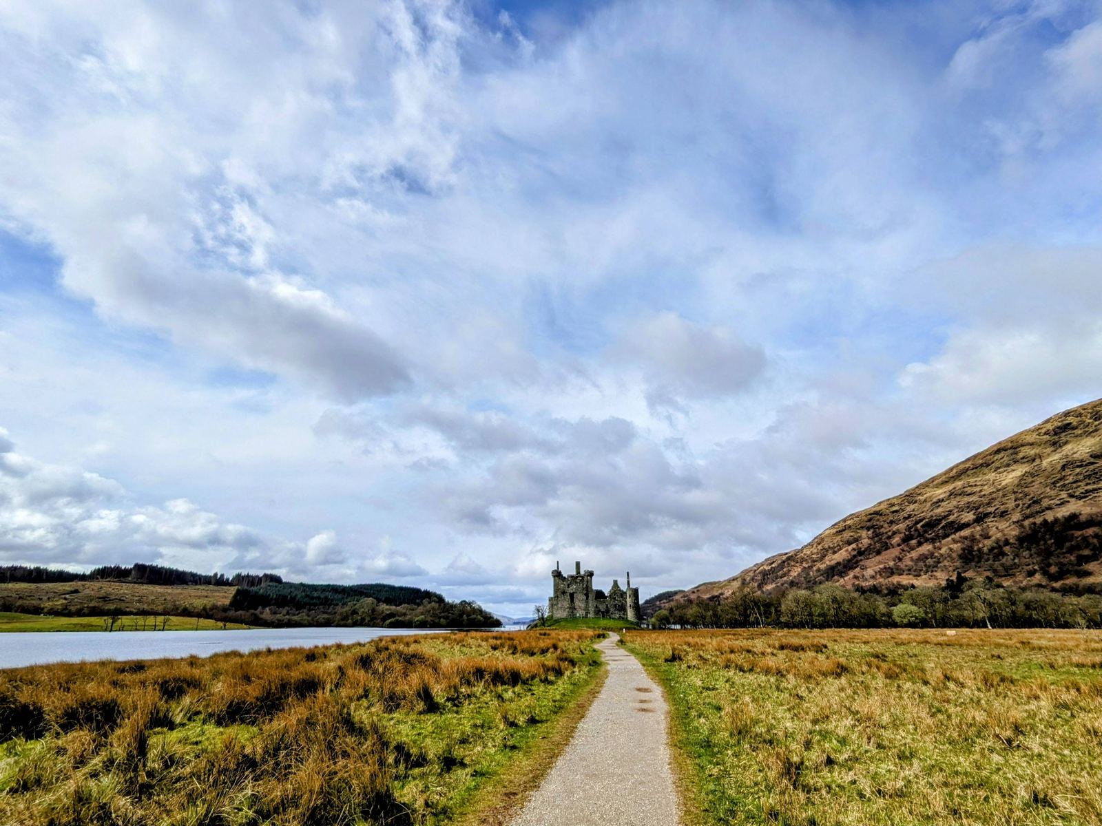 The footpath across the flat ground to Kilchurn Castle, snow-streaked mountains beyond.