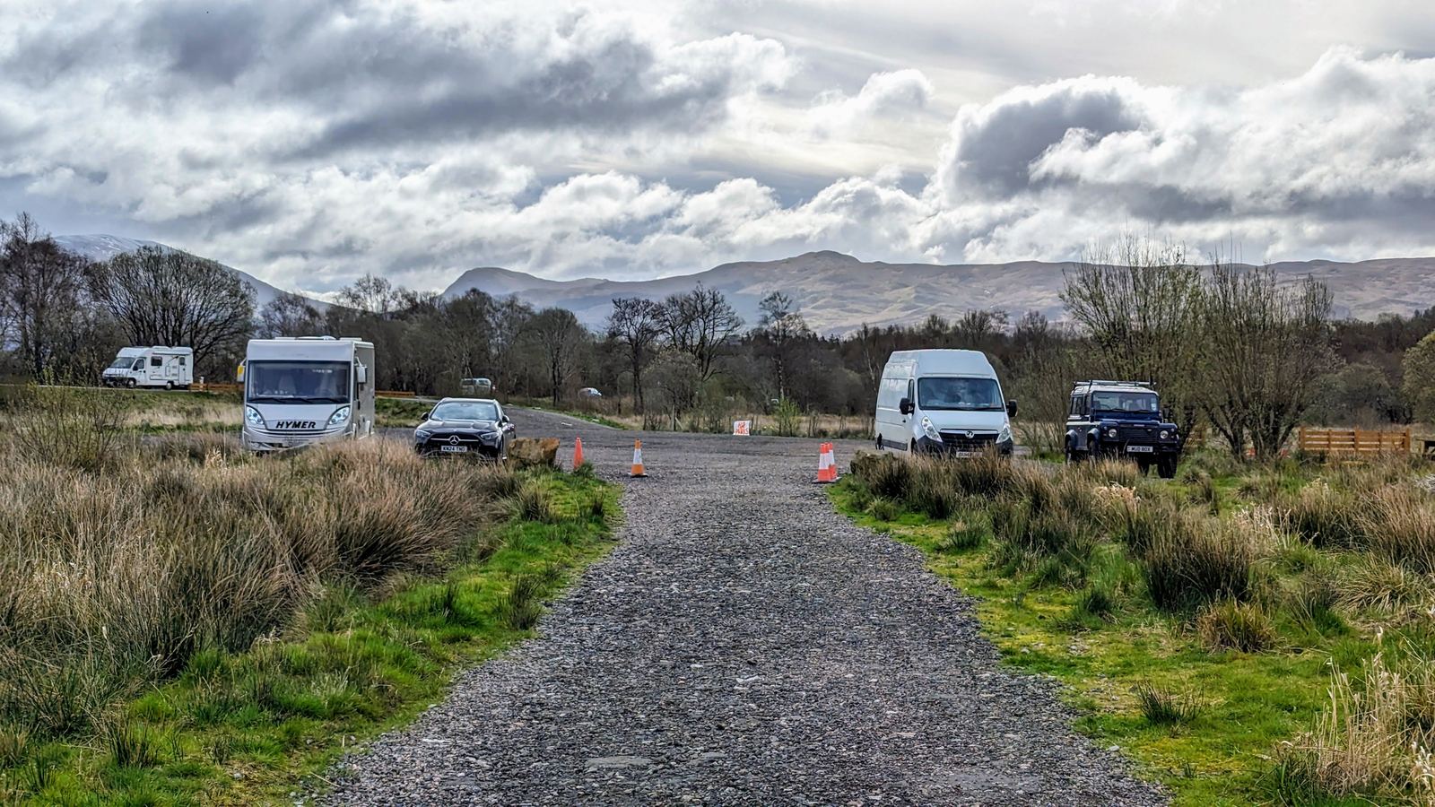 The gravel parking layby for Kilchurn Castle with campervans, hills beyond.