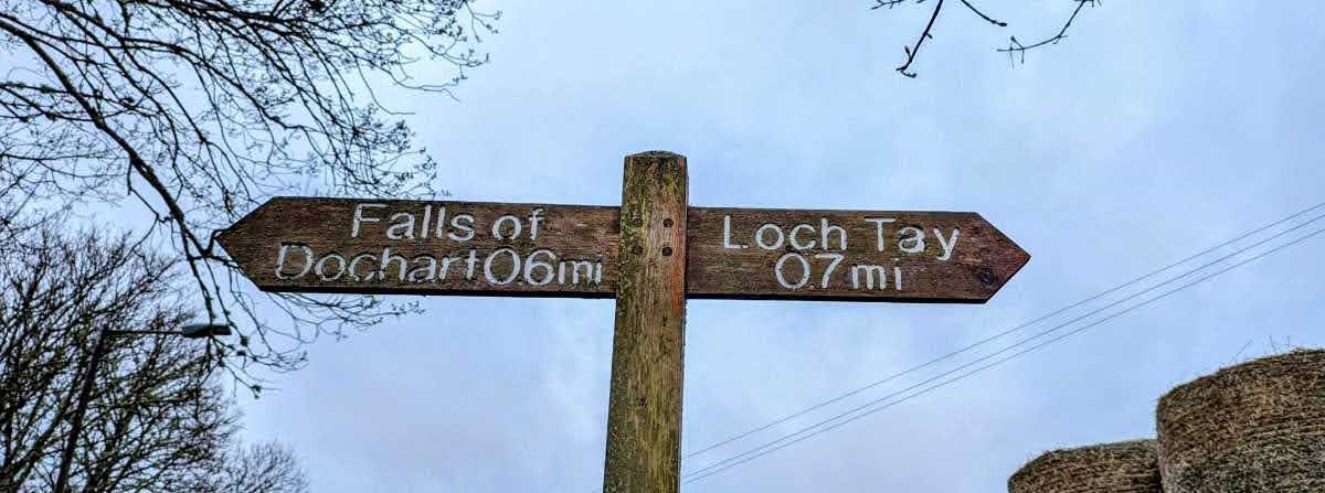 A wooden fingerpost signpost at Killin pointing to Falls of Dochart 0.6 miles and Loch Tay 0.7 miles.