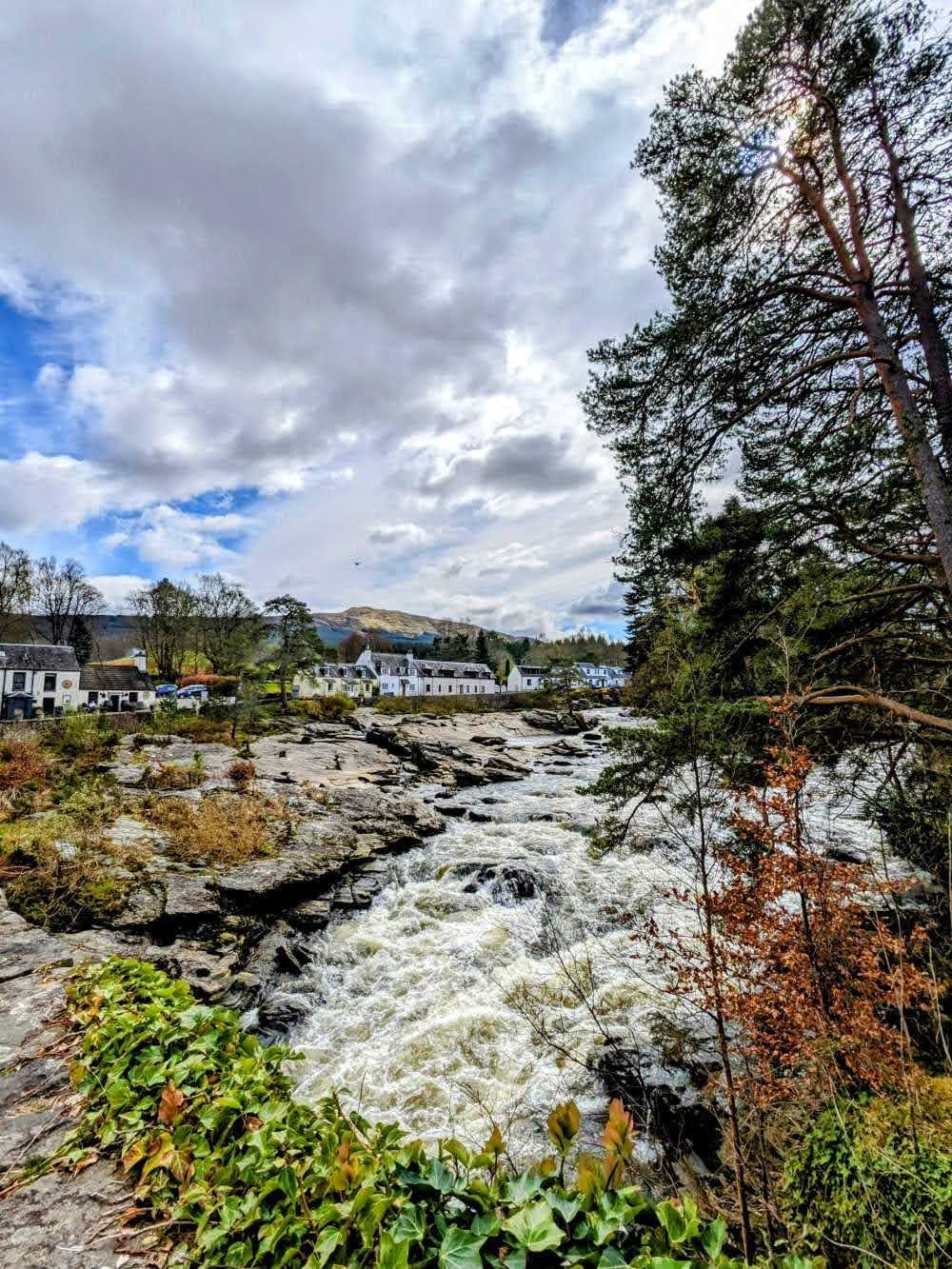 The Falls of Dochart in full spate at Killin, white water pouring over rock with the village and hills beyond.