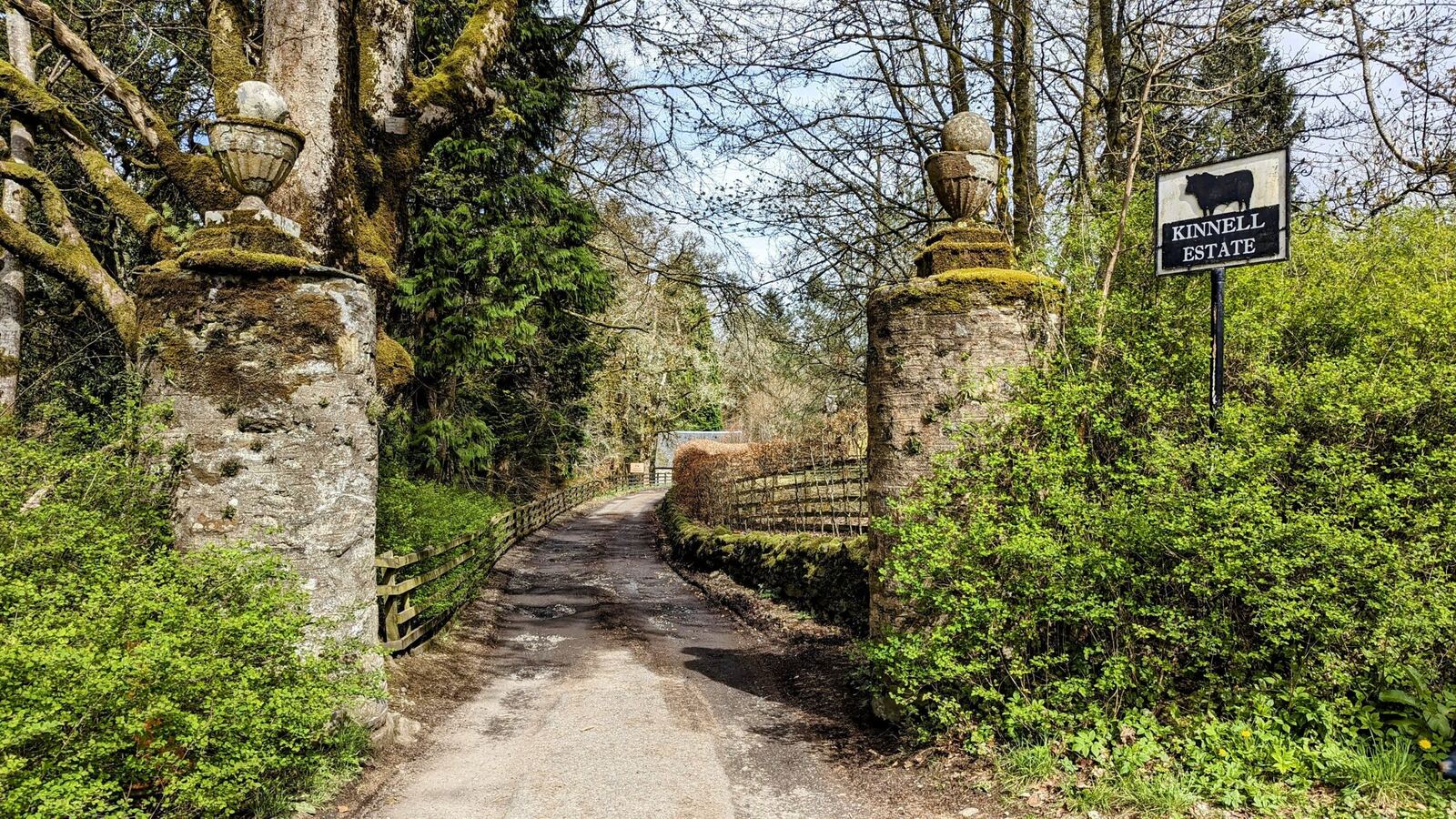 A path leading to the stone gateposts and Kinnell Estate sign near Killin, trees either side.