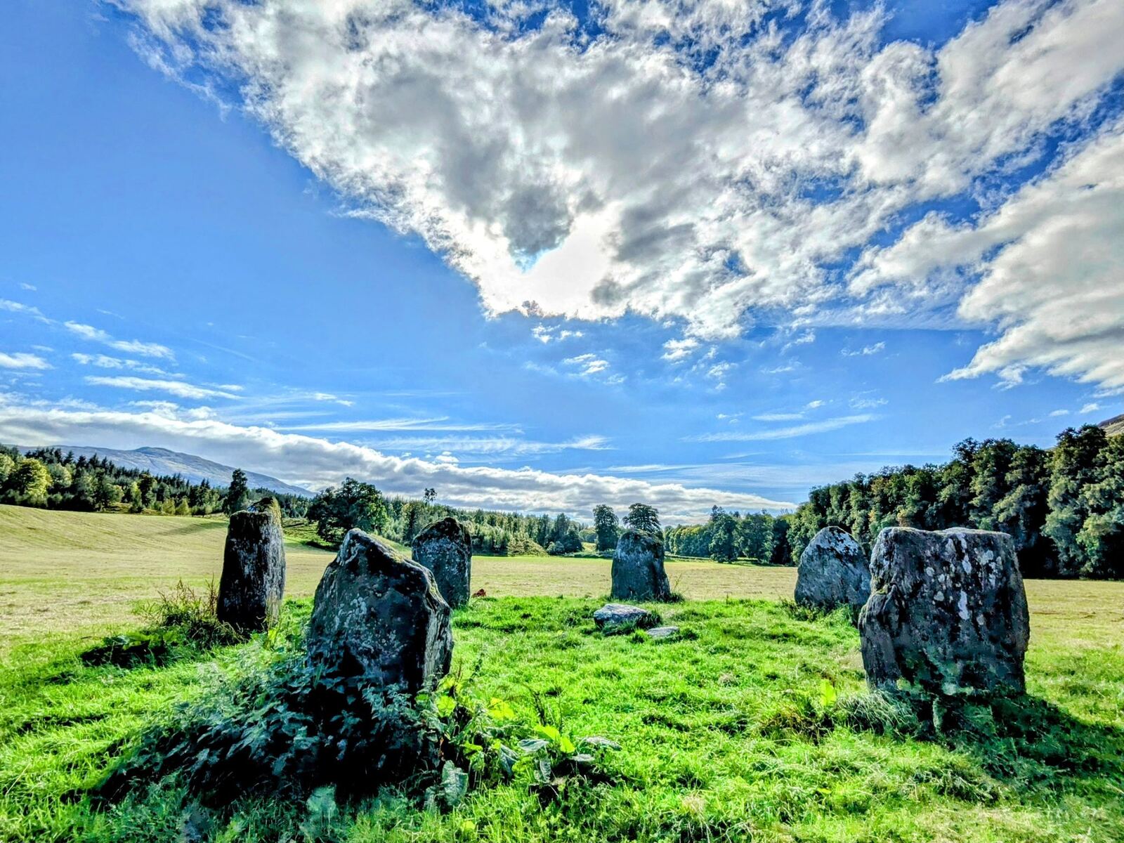 The Bronze Age Kinnell stone circle near Killin β six upright grey schist stones standing in a green field with trees and hills behind.