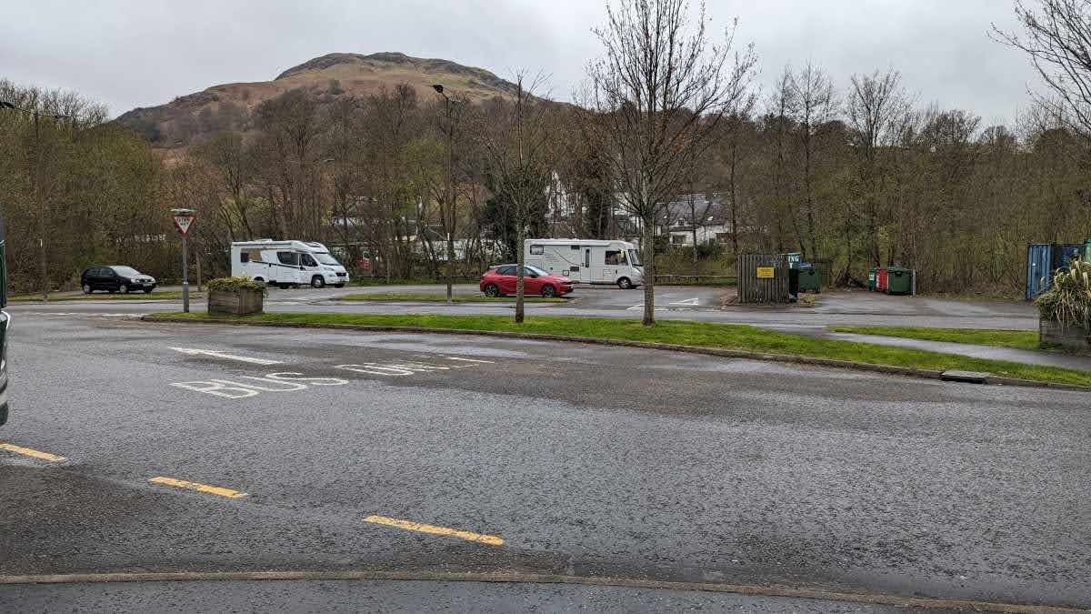 Motorhomes and campervans parked in the free car park at the back of Killin, hills behind.