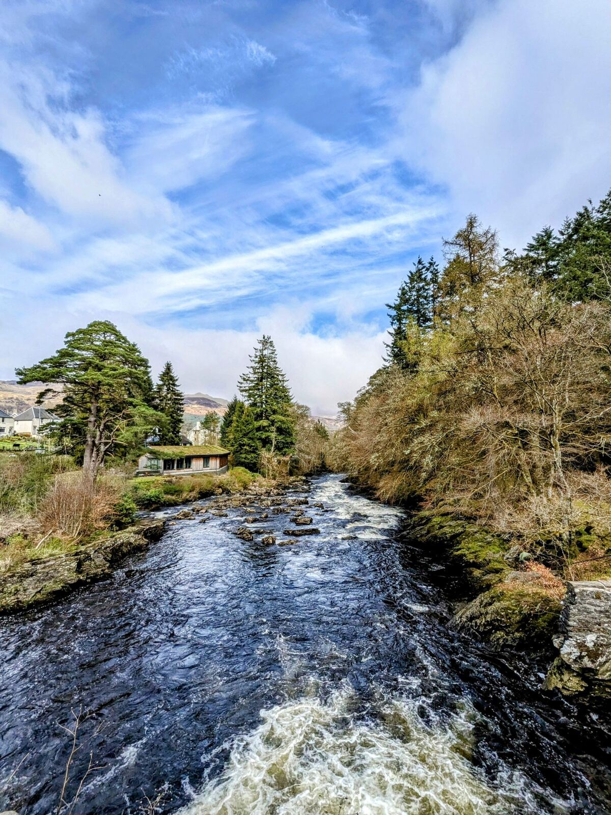 The River Dochart rushing past the edge of Killin village under a blue sky.