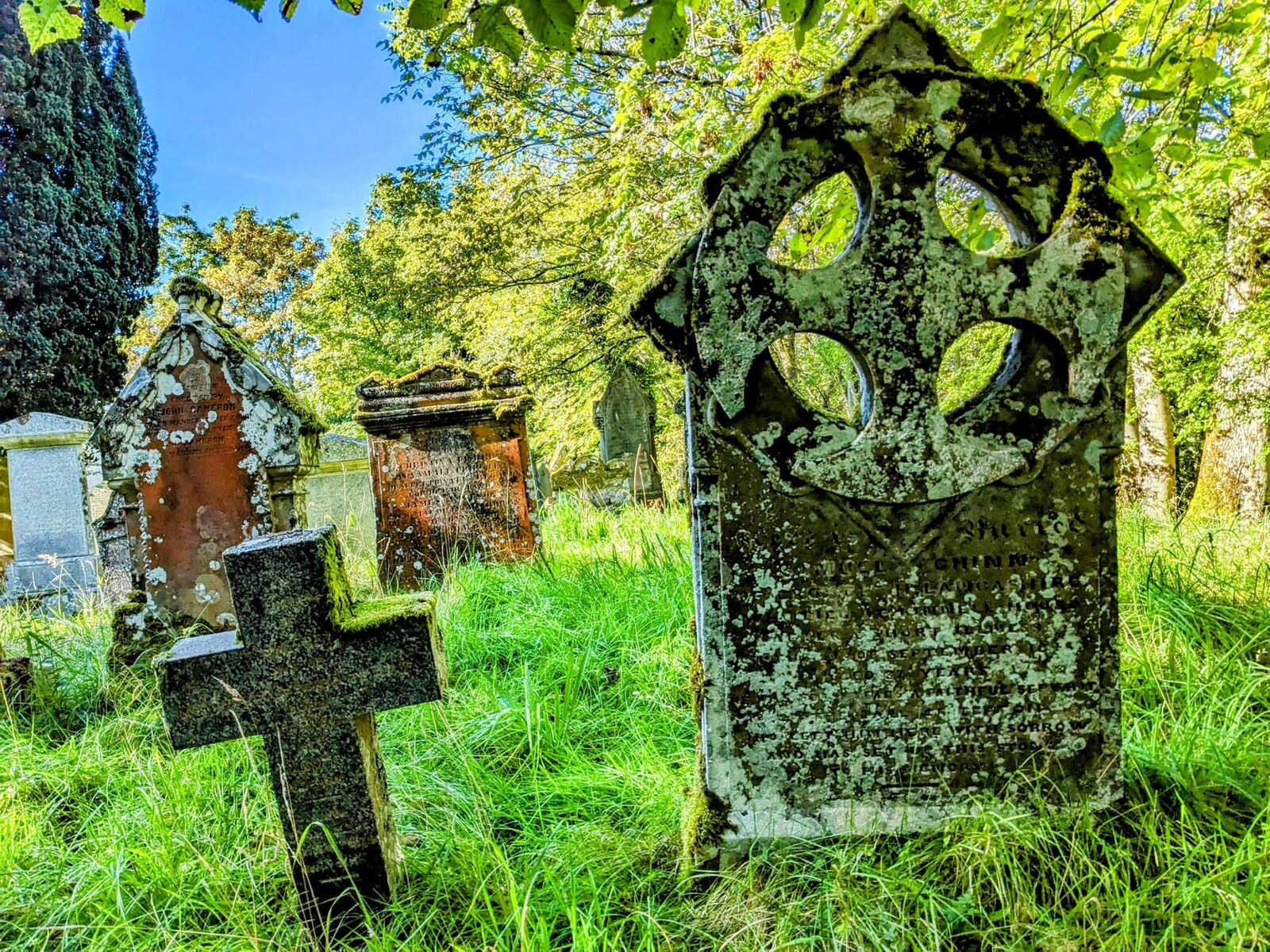 A carved Celtic cross gravestone standing in the green old kirkyard at Killin.